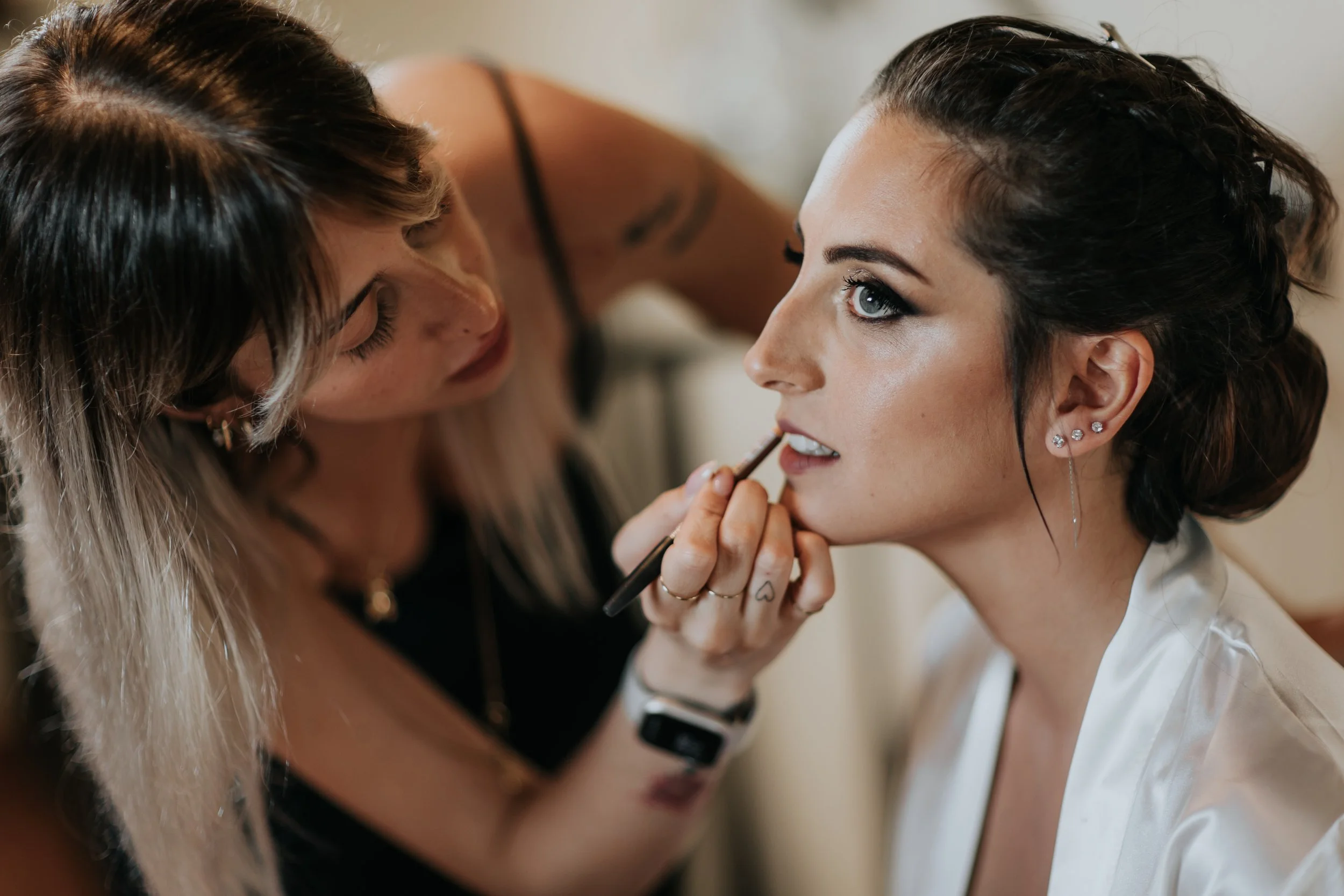 Una donna con l'orecchino alla cartilagine riceve un trucco con un pennello da un'altra donna