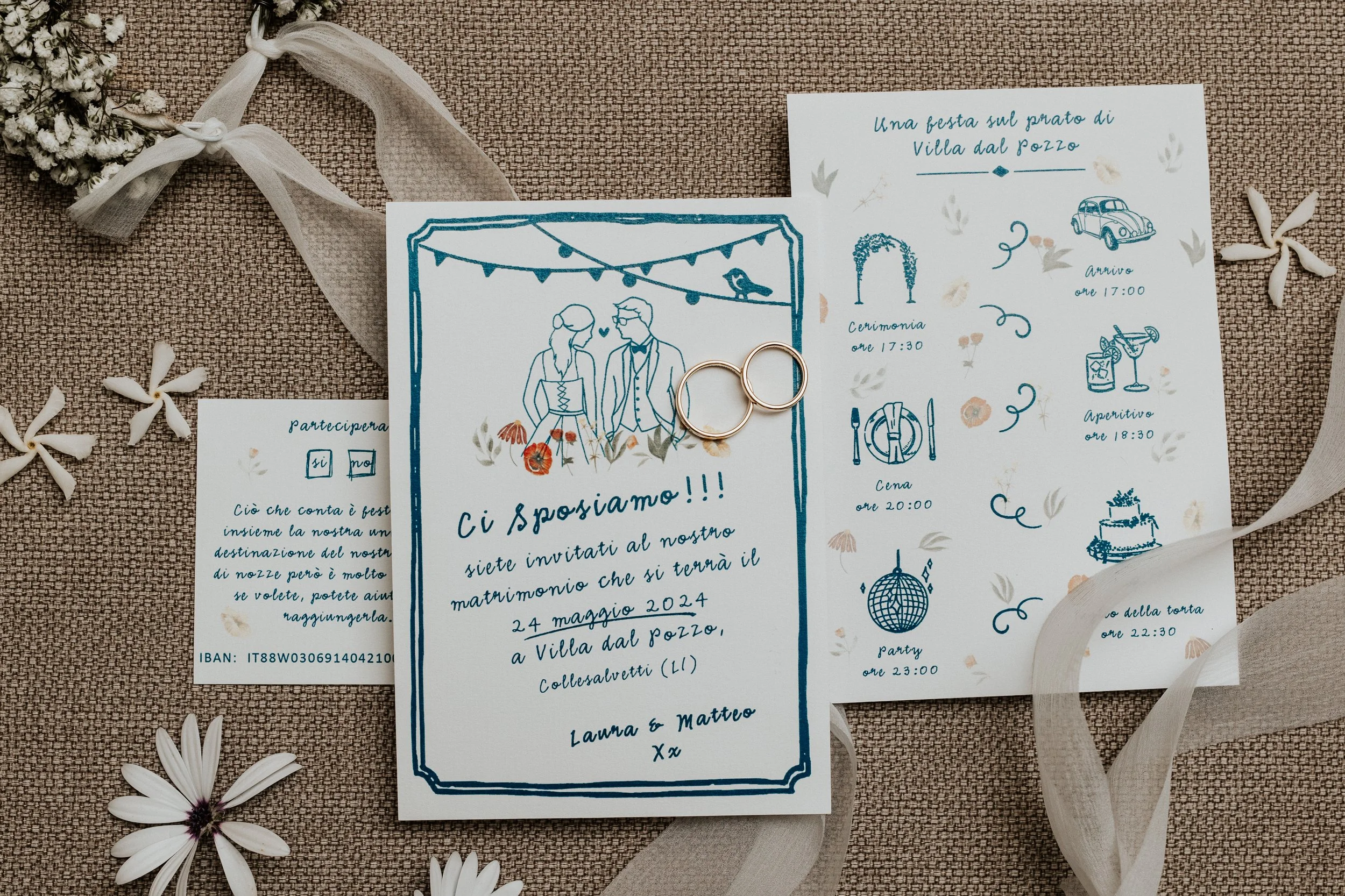 Biglietti di invito di matrimonio decorati con disegni di elementi festivi, anelli dorati sovrapposti, fiori e nastri su sfondo in tessuto, con ispirazione romantica e festiva.