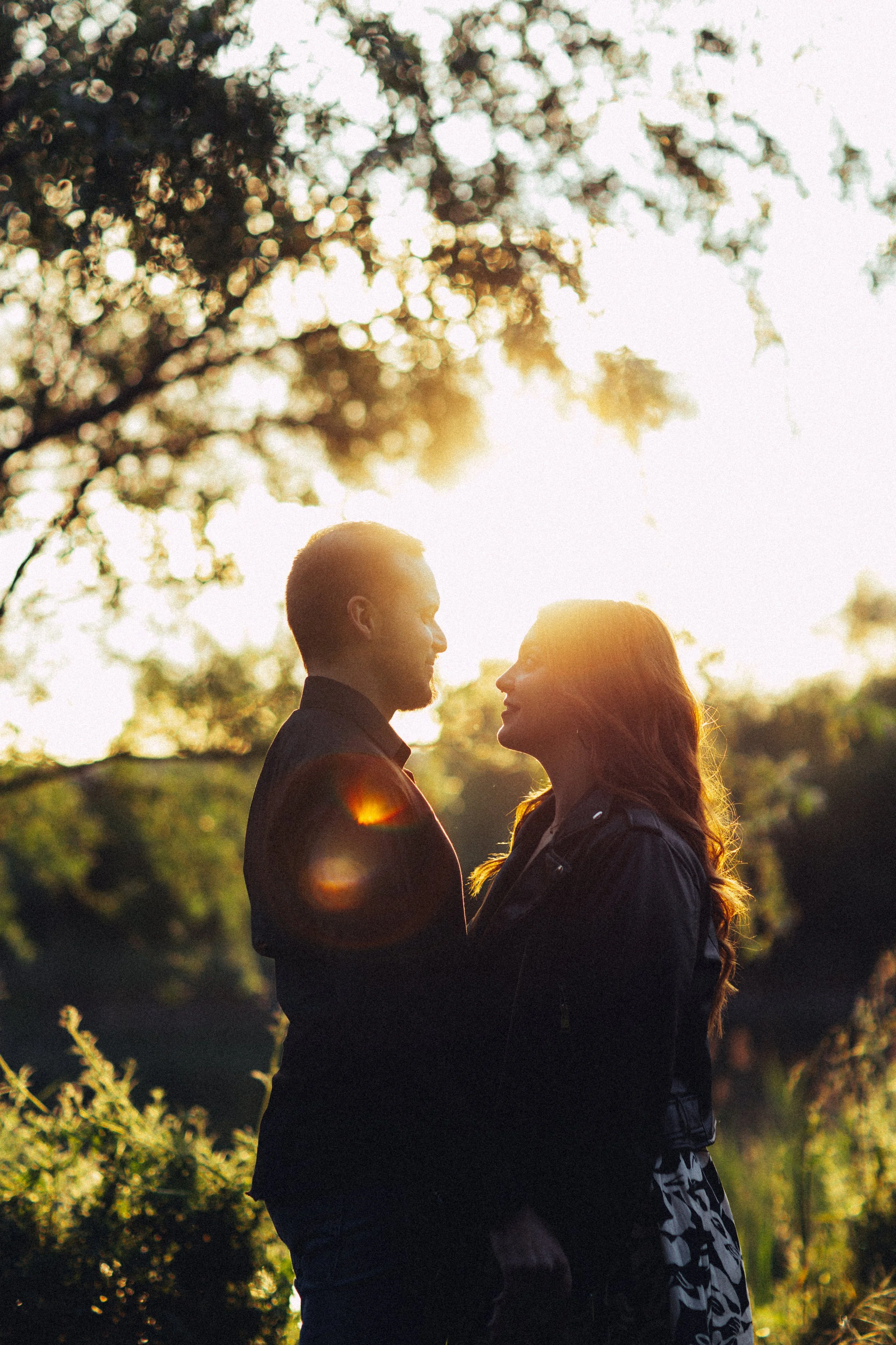 Una coppia si guarda negli occhi con il sole al tramonto alle spalle, circondata da alberi e natura.