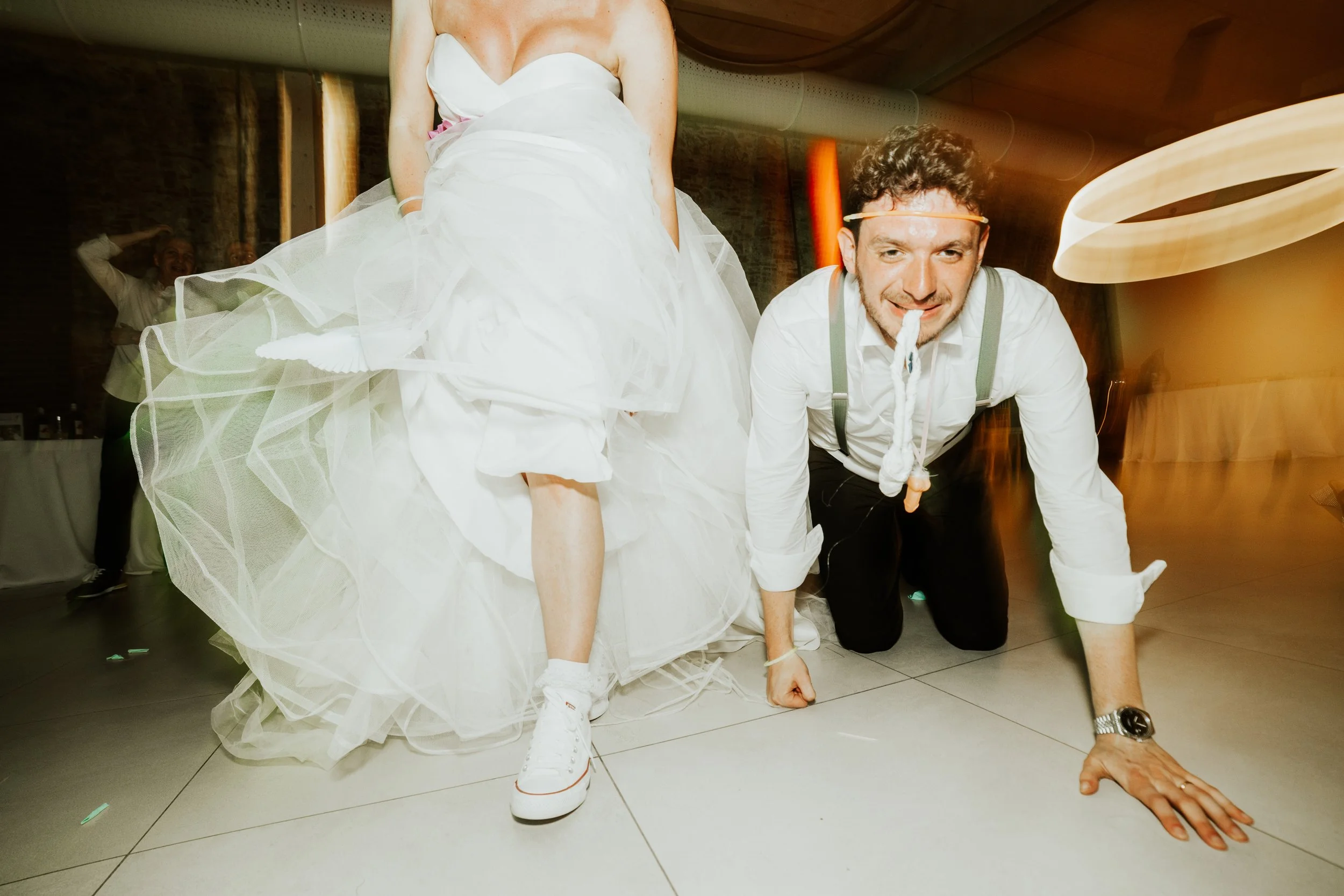 Uomo che si mimetizza in un costume di sposa con scarpe da ginnastica in un matrimonio, mentre è in posizione a quattro zampe sul pavimento.