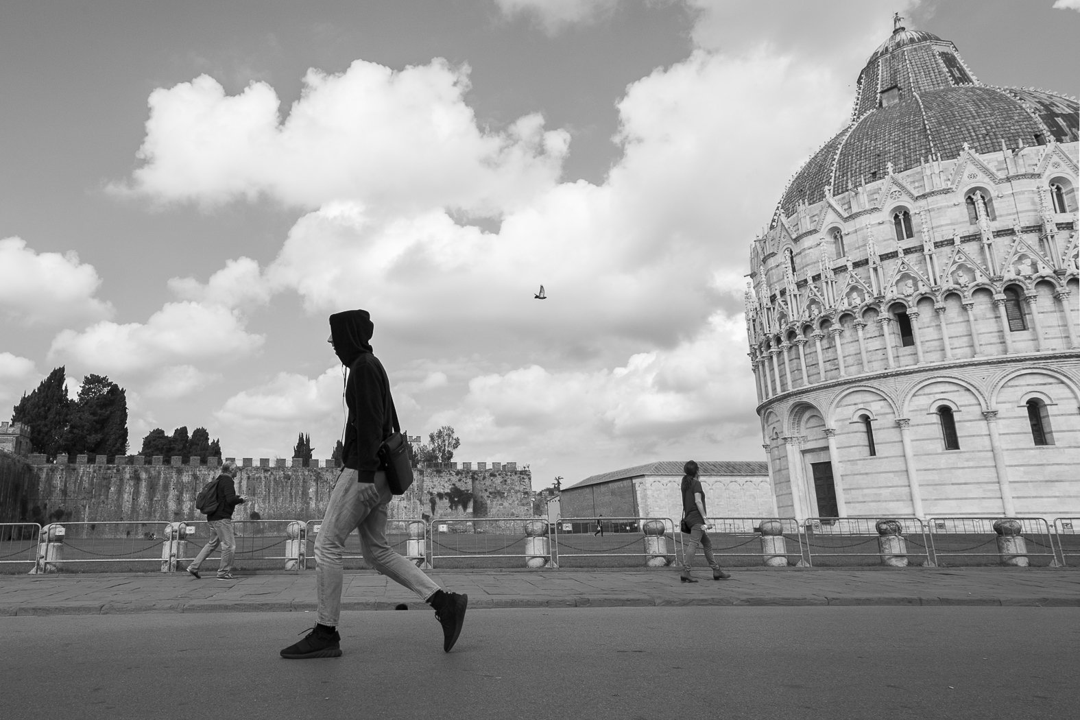 Persone che camminano lungo una strada vicino a un edificio storico, il Duomo di Pisa, con un cielo nuvoloso