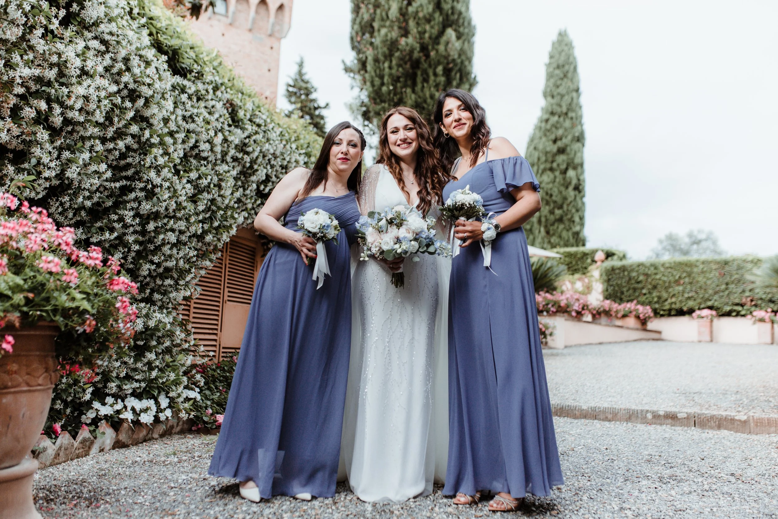 Tre donne in abiti da sera, con bouquet di fiori, sorridenti e posate in un giardino.