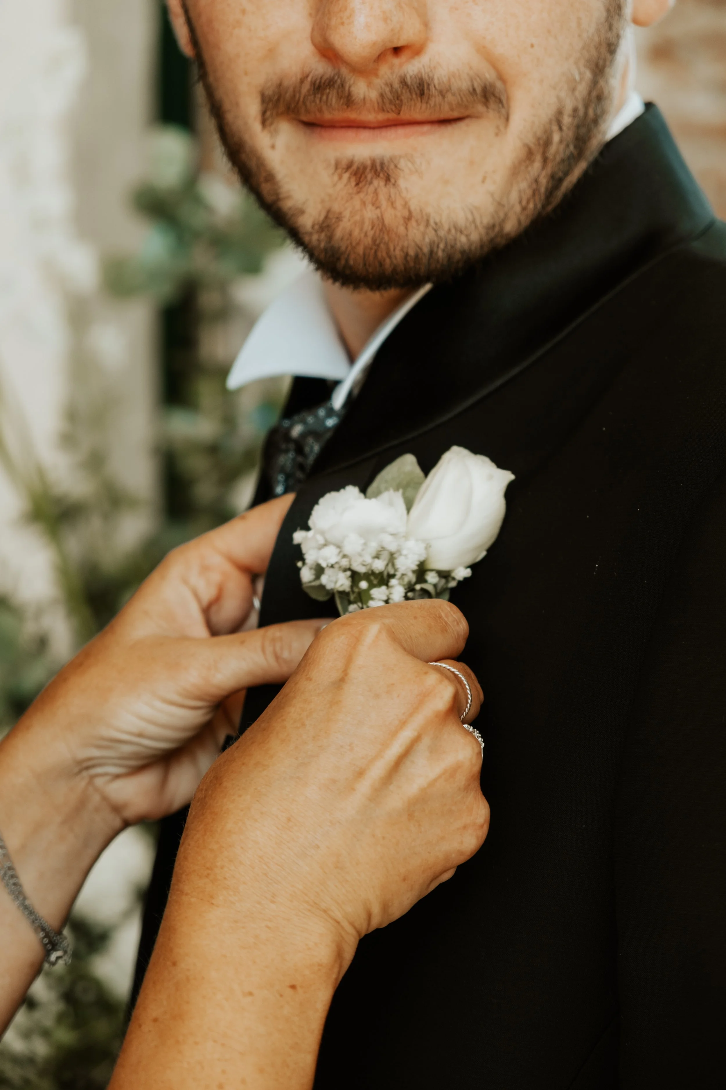 Persona che indossa un abito da uomo, con una donna che sistema un fiore sulla sue giacca, probabilmente per un matrimonio.