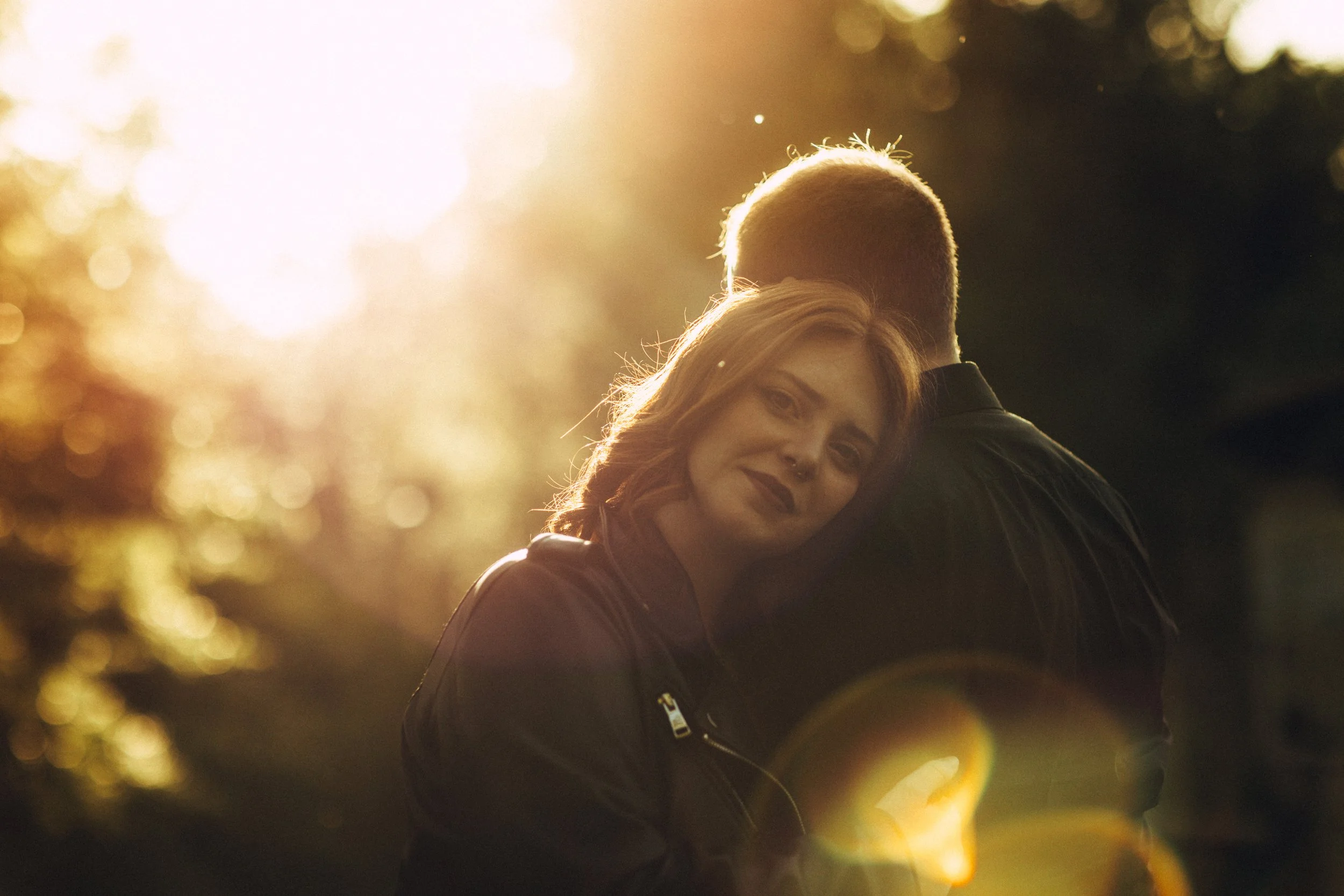 Una donna abbraccia un uomo in un tramonto caldo, con la luce del sole che crea un effetto di bagliore e lens flare.