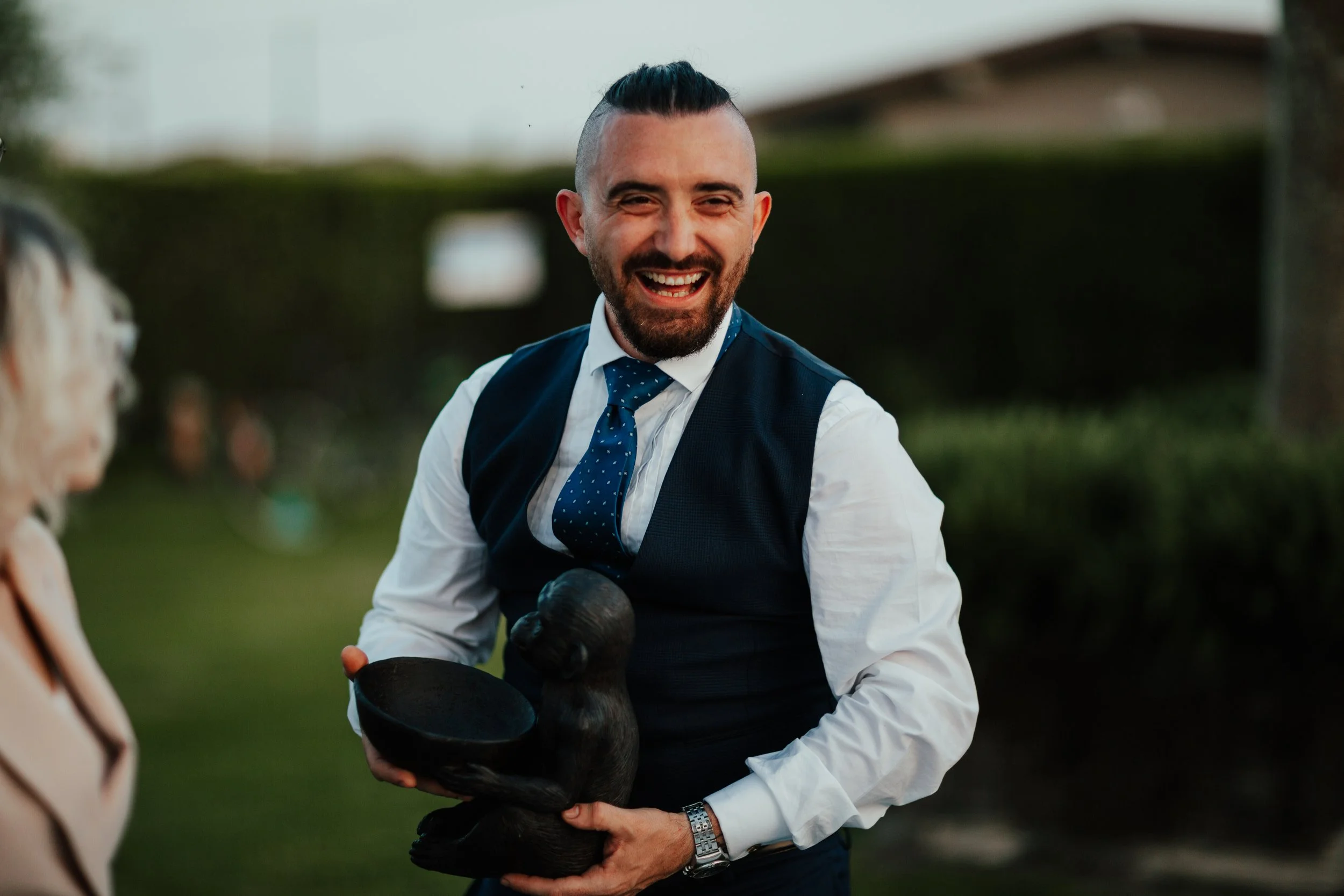 Uomo sorridente con abito e cravatta blu che tiene un basamento decorativo a forma di castoro in mano durante un evento all'aperto
