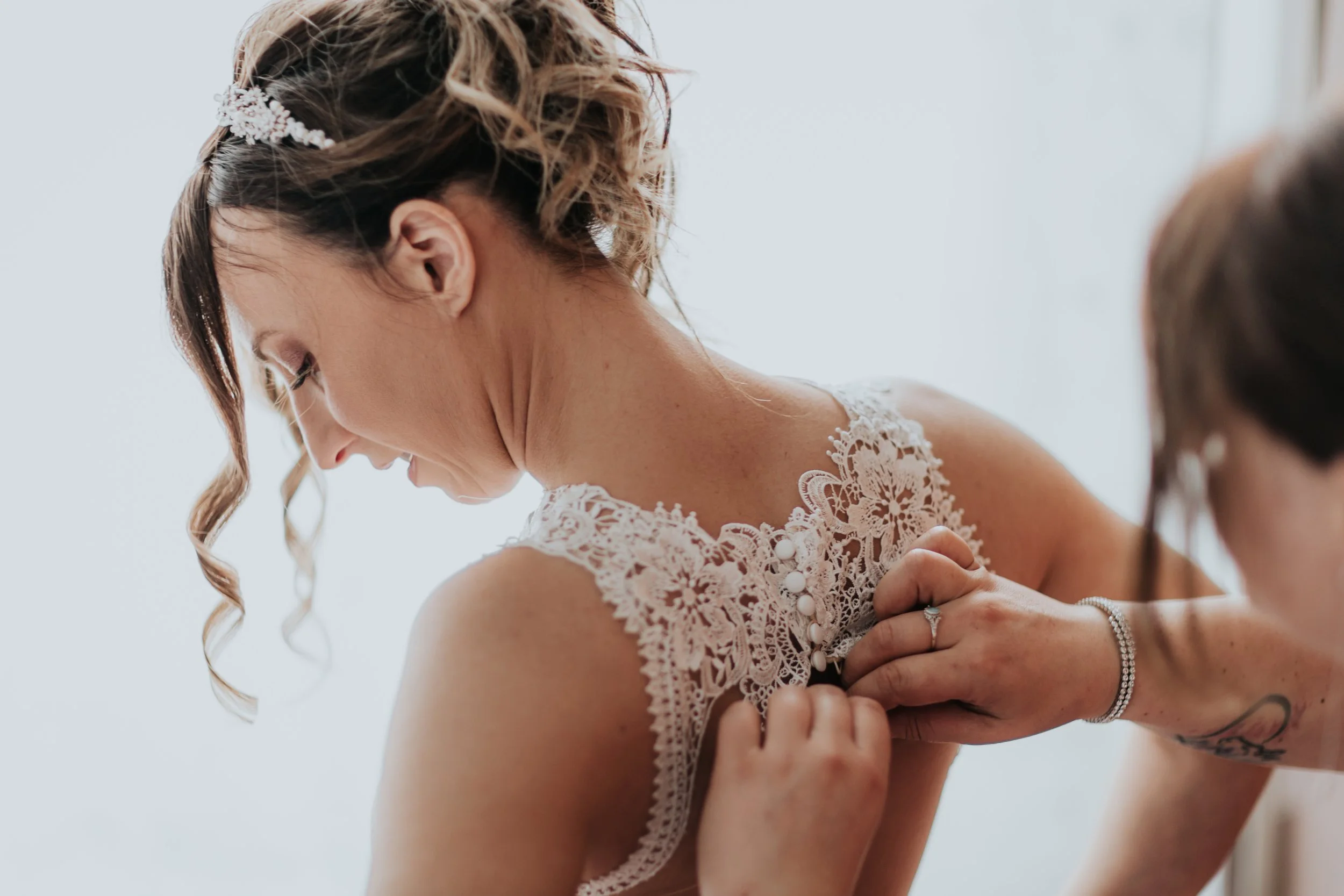 Una sposa indossa il vestito da sposa mentre una persona le aiuta a sistemarlo.