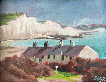 Waterfront scene with colorful houses, green bushes, and distant mountains under a blue sky with some clouds.