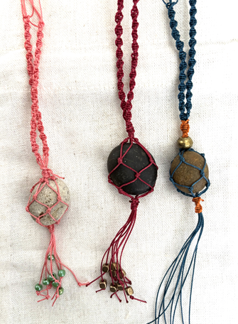 Three handmade necklaces with wire-wrapped stones and braided cords in pink, red, and blue, displayed on a light fabric background.