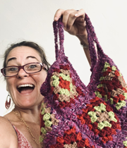 Smiling woman holding a colorful knitted bag with floral patterns.