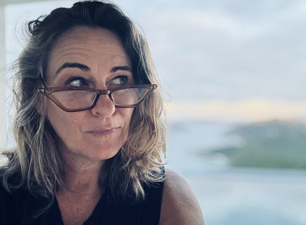 A woman with glasses looking to the side with a scenic outdoor background.