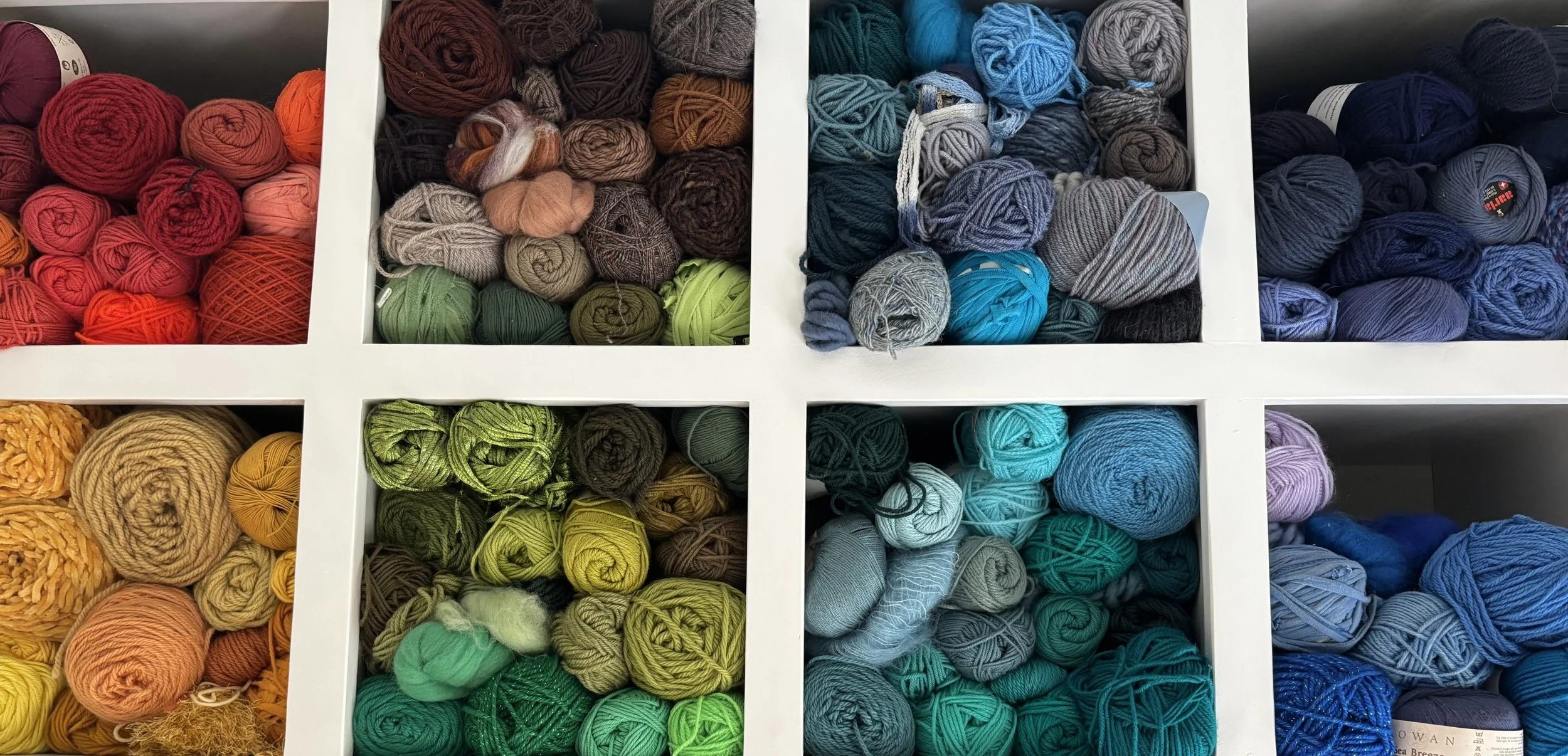 Shelf containing multiple compartments filled with balls of yarn in various colors including red, orange, green, blue, gray, purple, and yellow, organized by color.