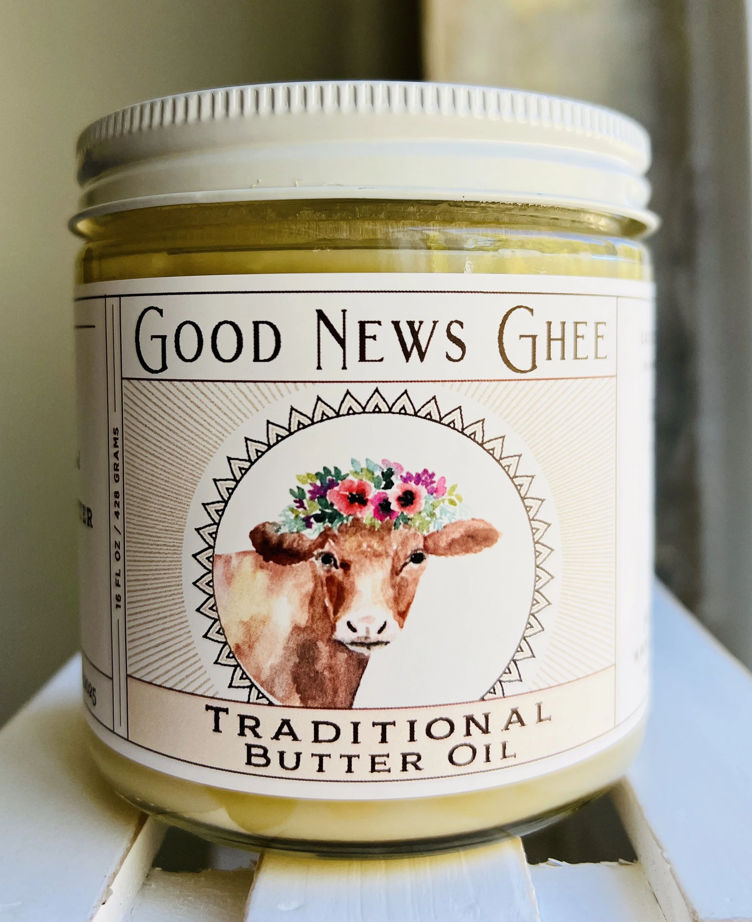 A jar of Good News Ghee traditional butter oil featuring a cow with a floral crown on the label.