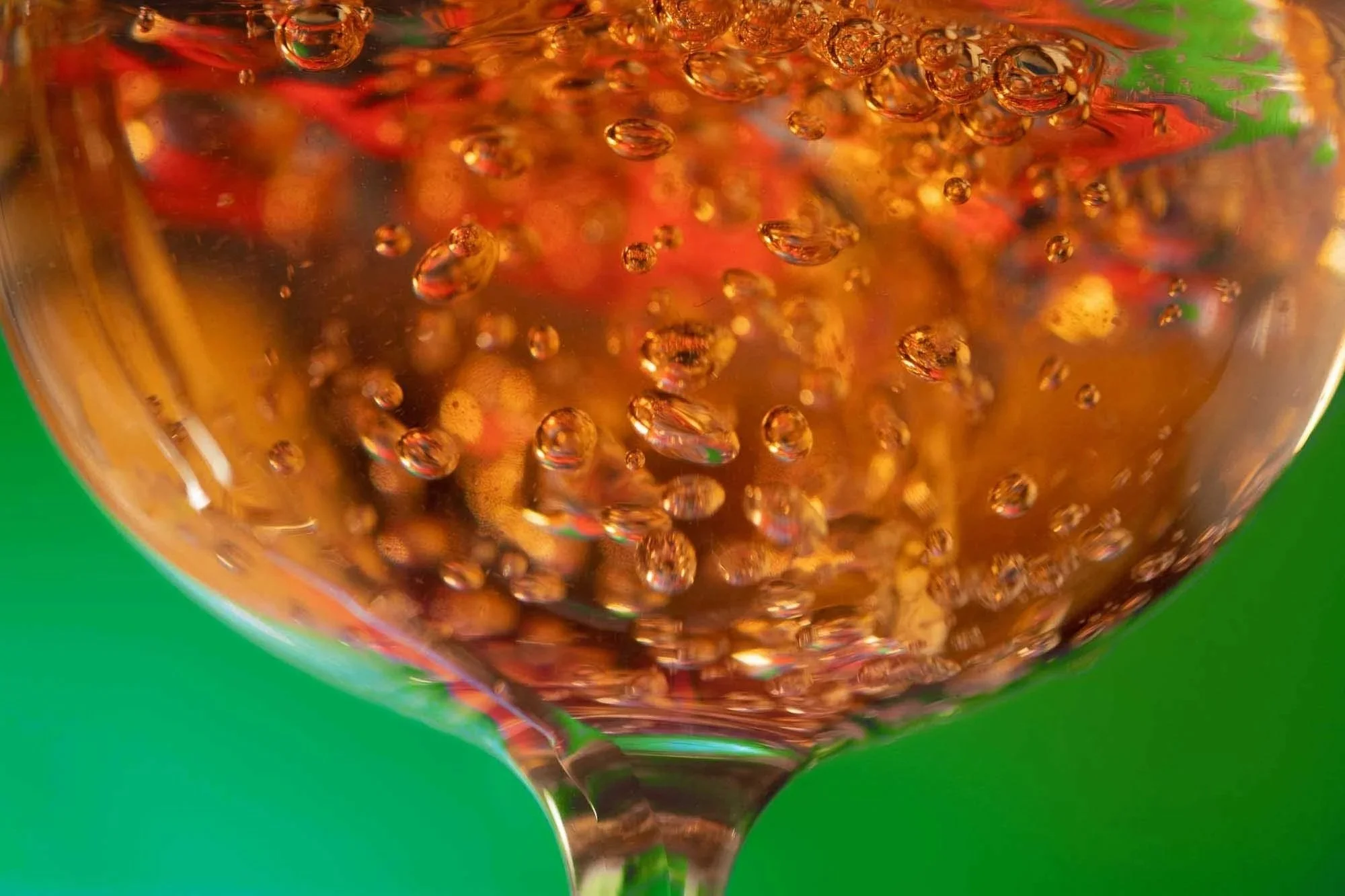Close-up of bubbles inside a glass of amber-colored soda against a green background.