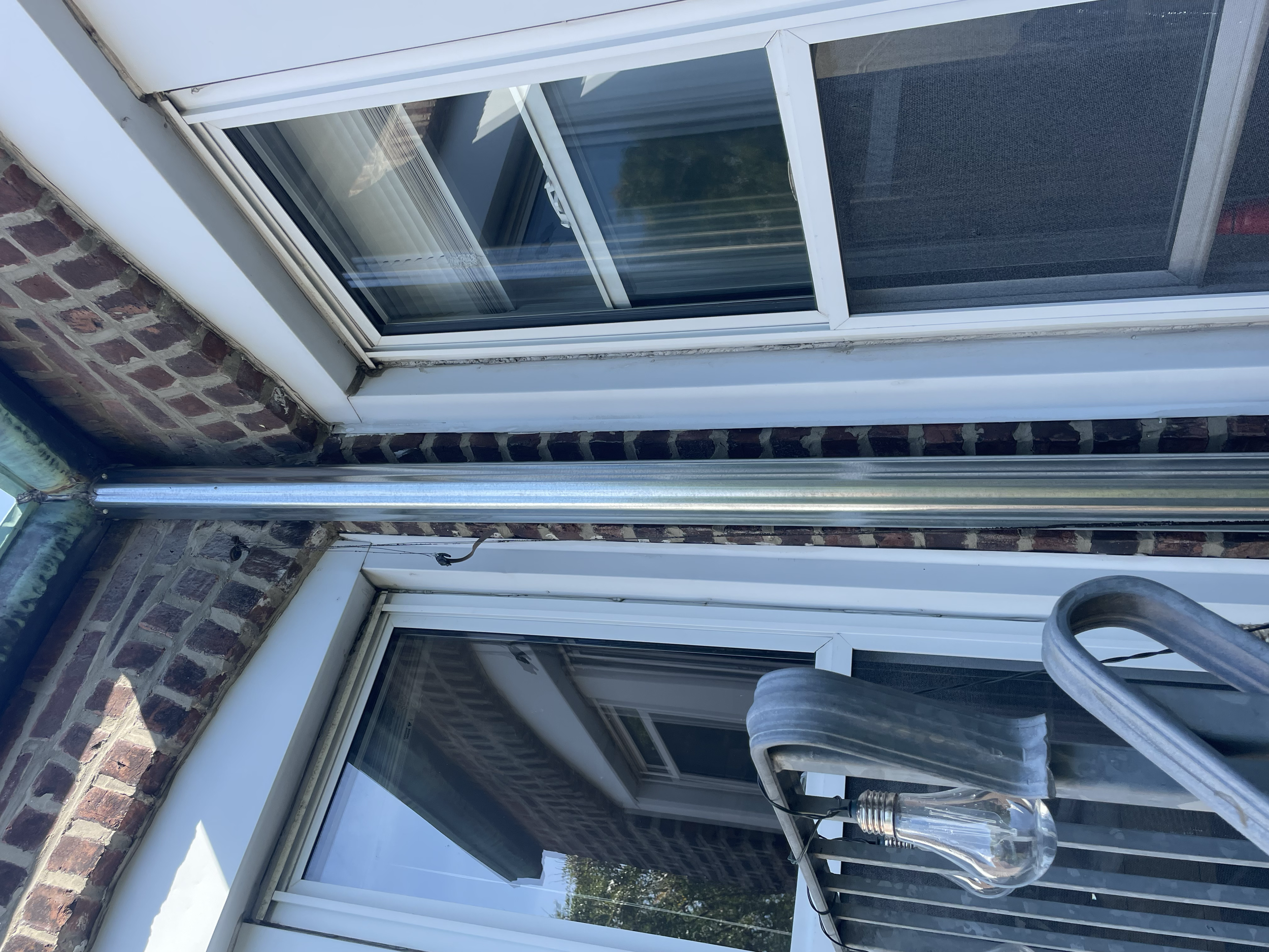 Exterior view of brick wall with two white-framed windows, metal pipe, and outdoor light fixture.