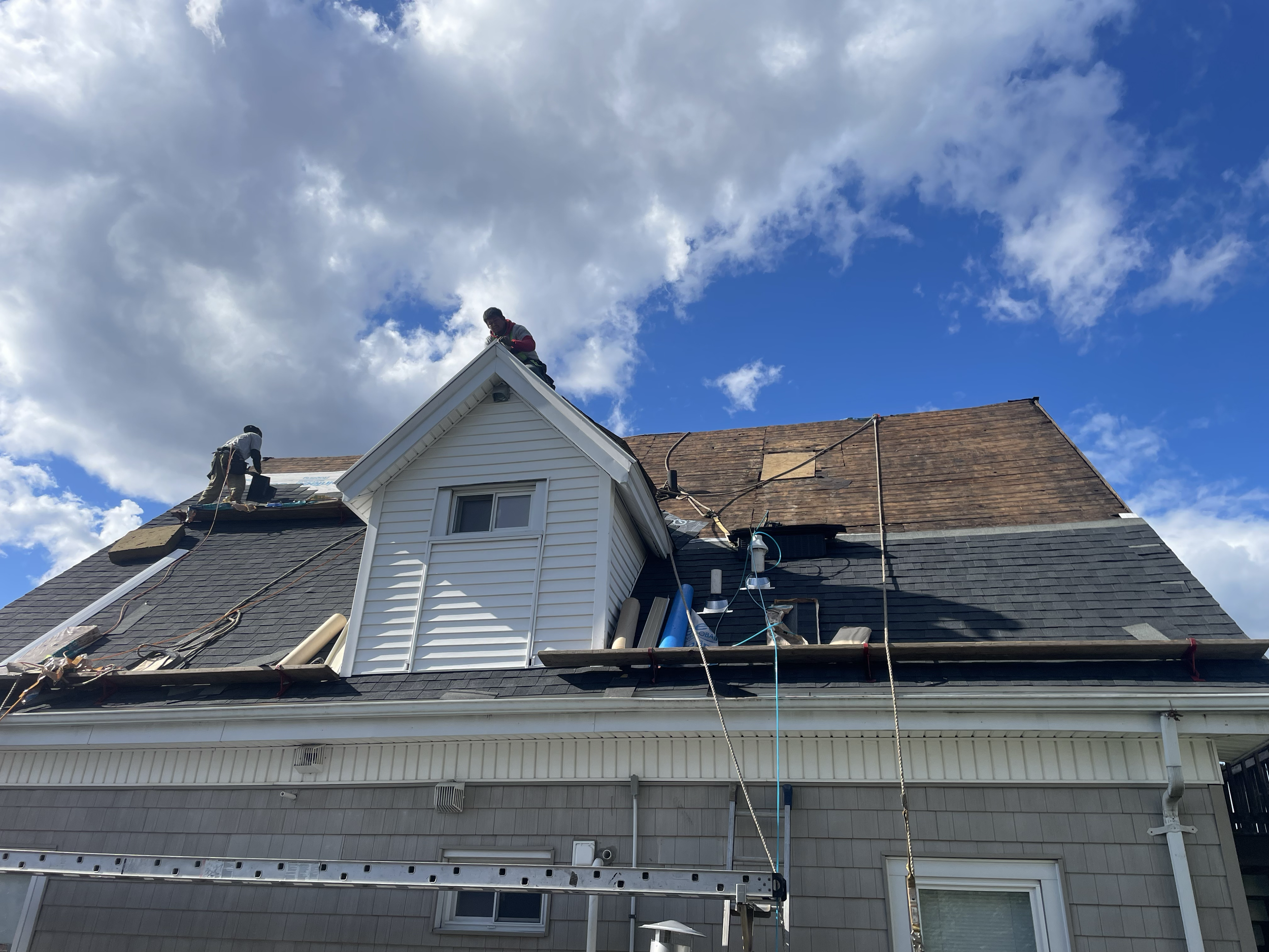 Roof repair in progress with two workers, shingles removed, blue sky background.