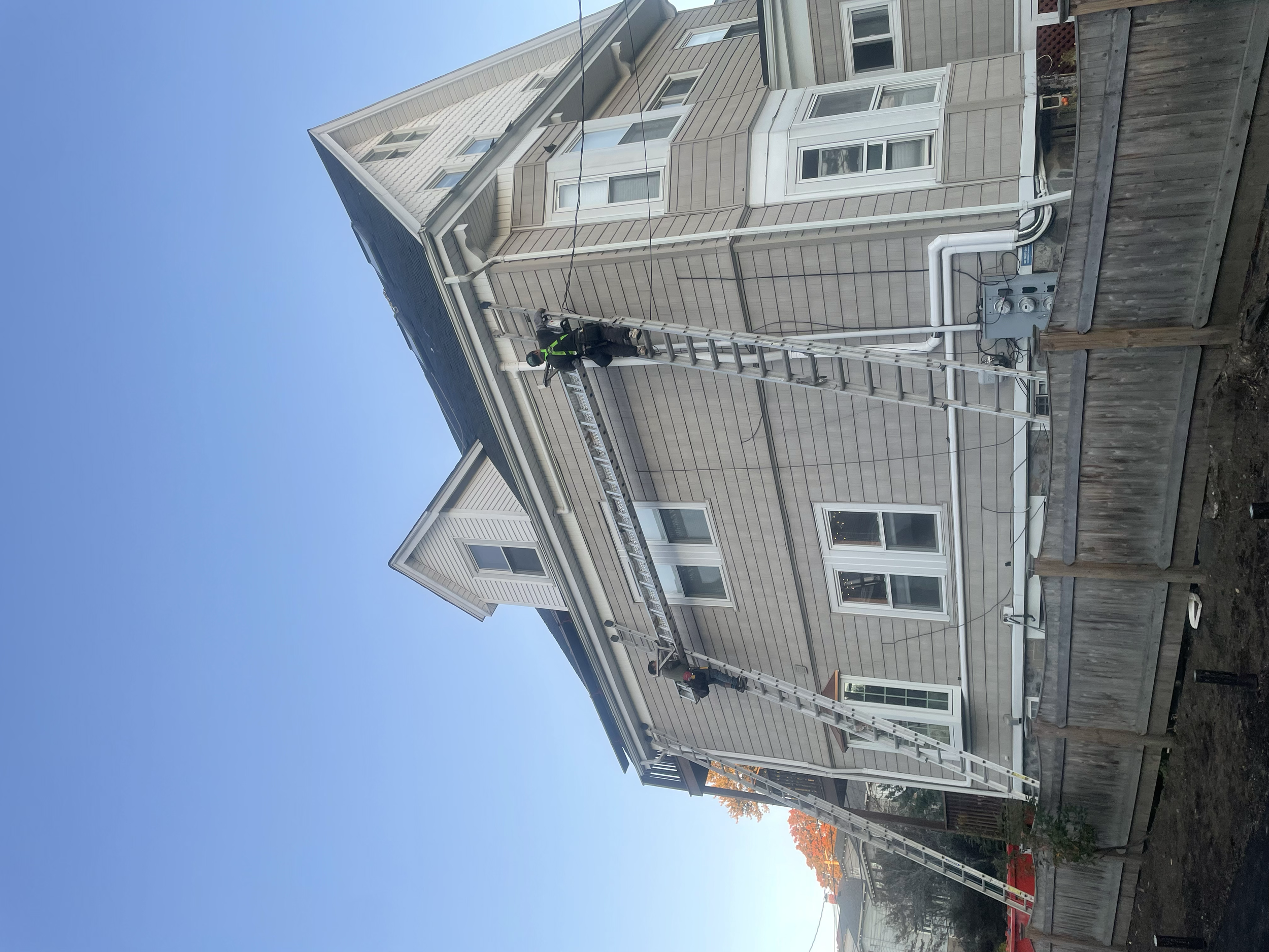 Workers on a ladder performing maintenance on a three-story residential building exterior with beige siding.