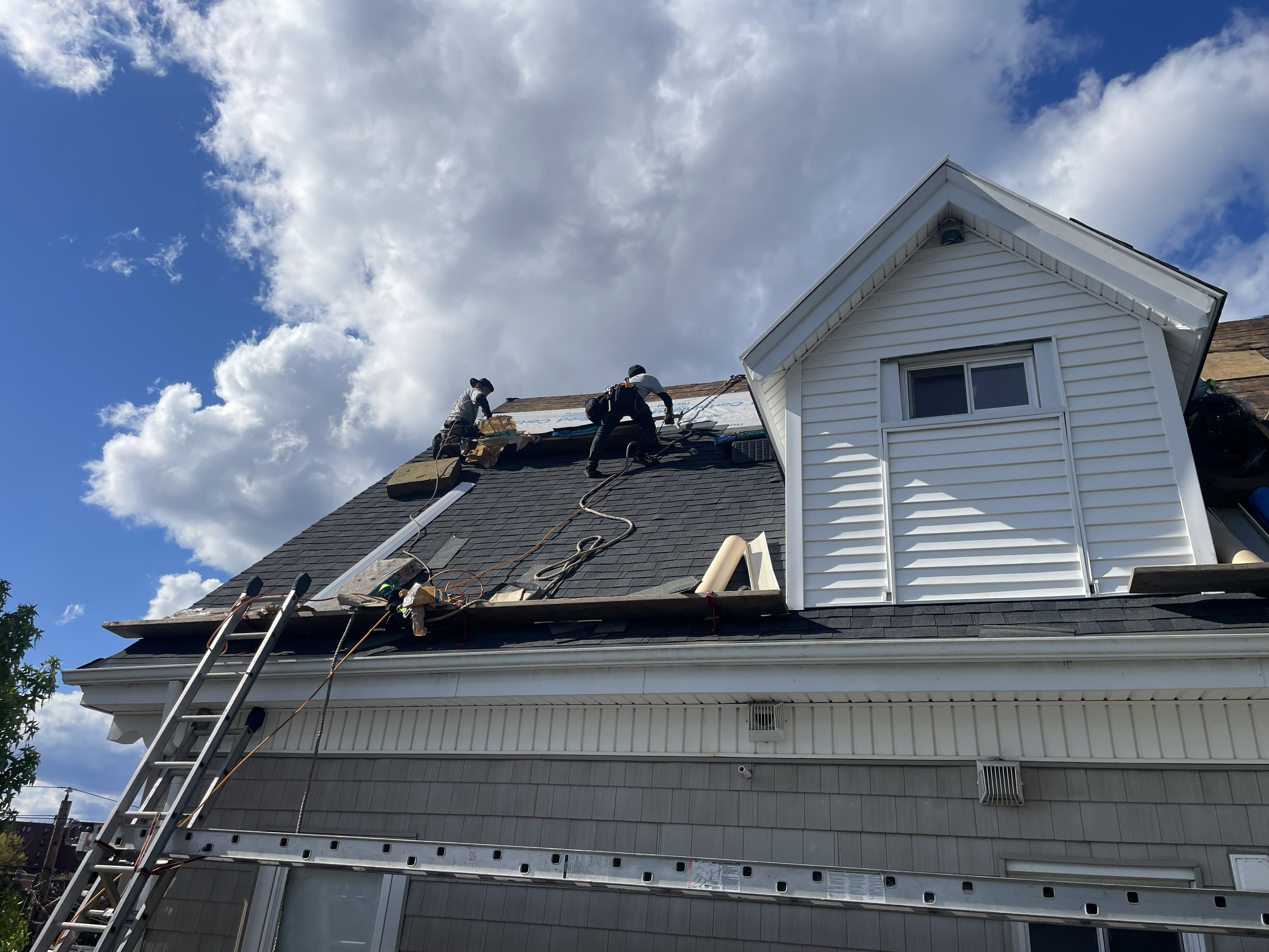 Roofers repairing shingles on a house under a partly cloudy sky.