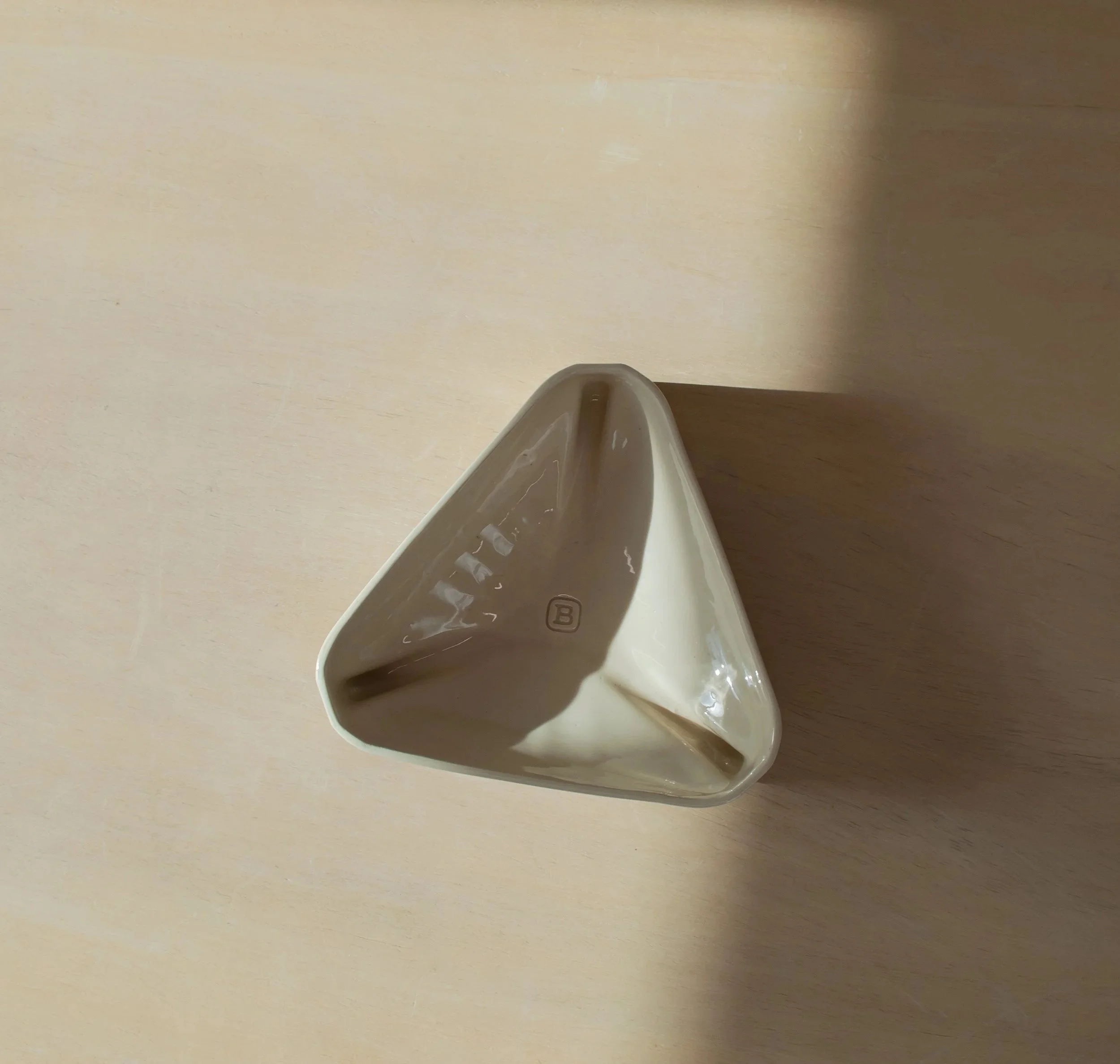 Top view of a triangular ceramic bowl with glossy cream glaze
