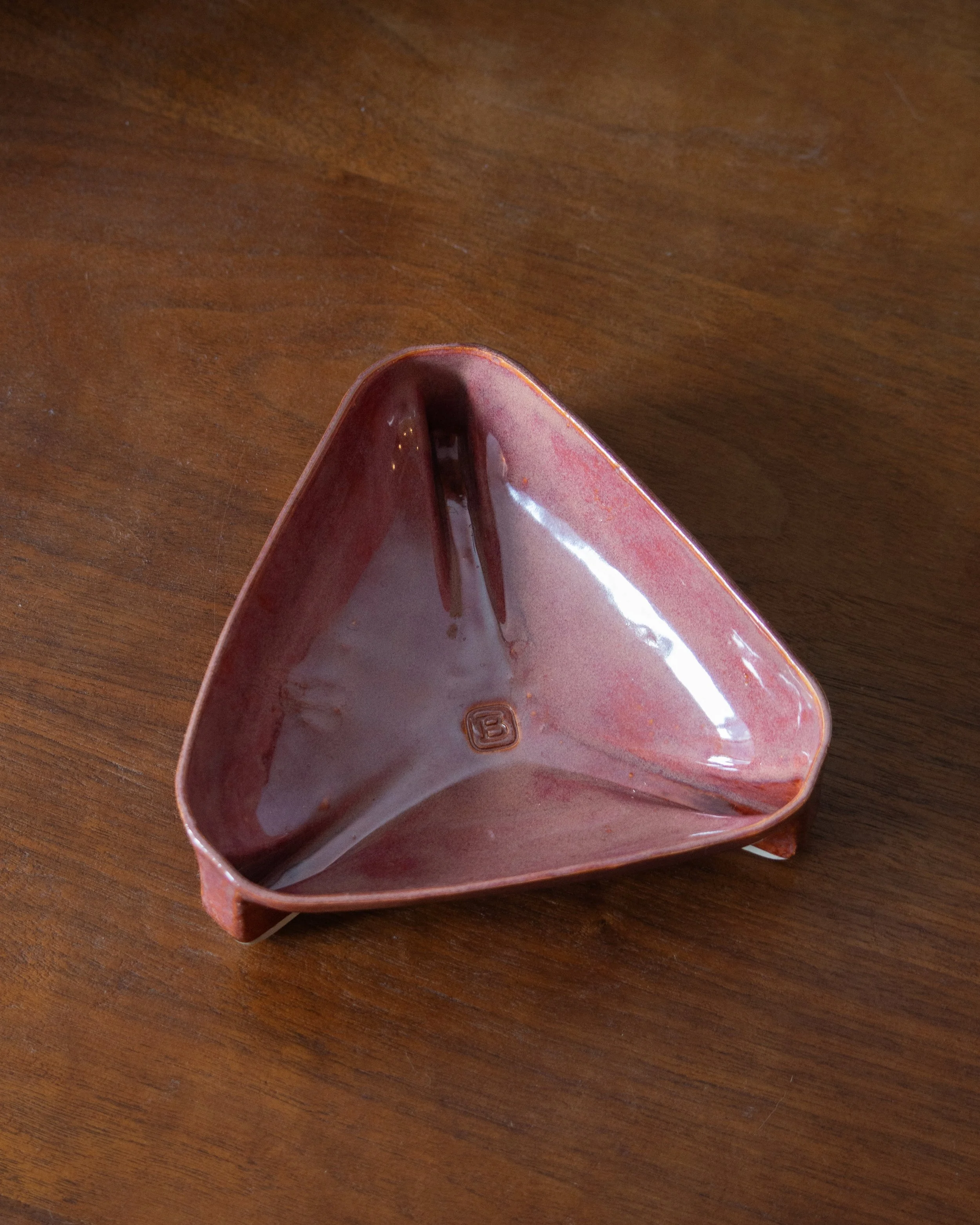 Top view of a triangular ceramic bowl with glossy pink glaze on wooden surface