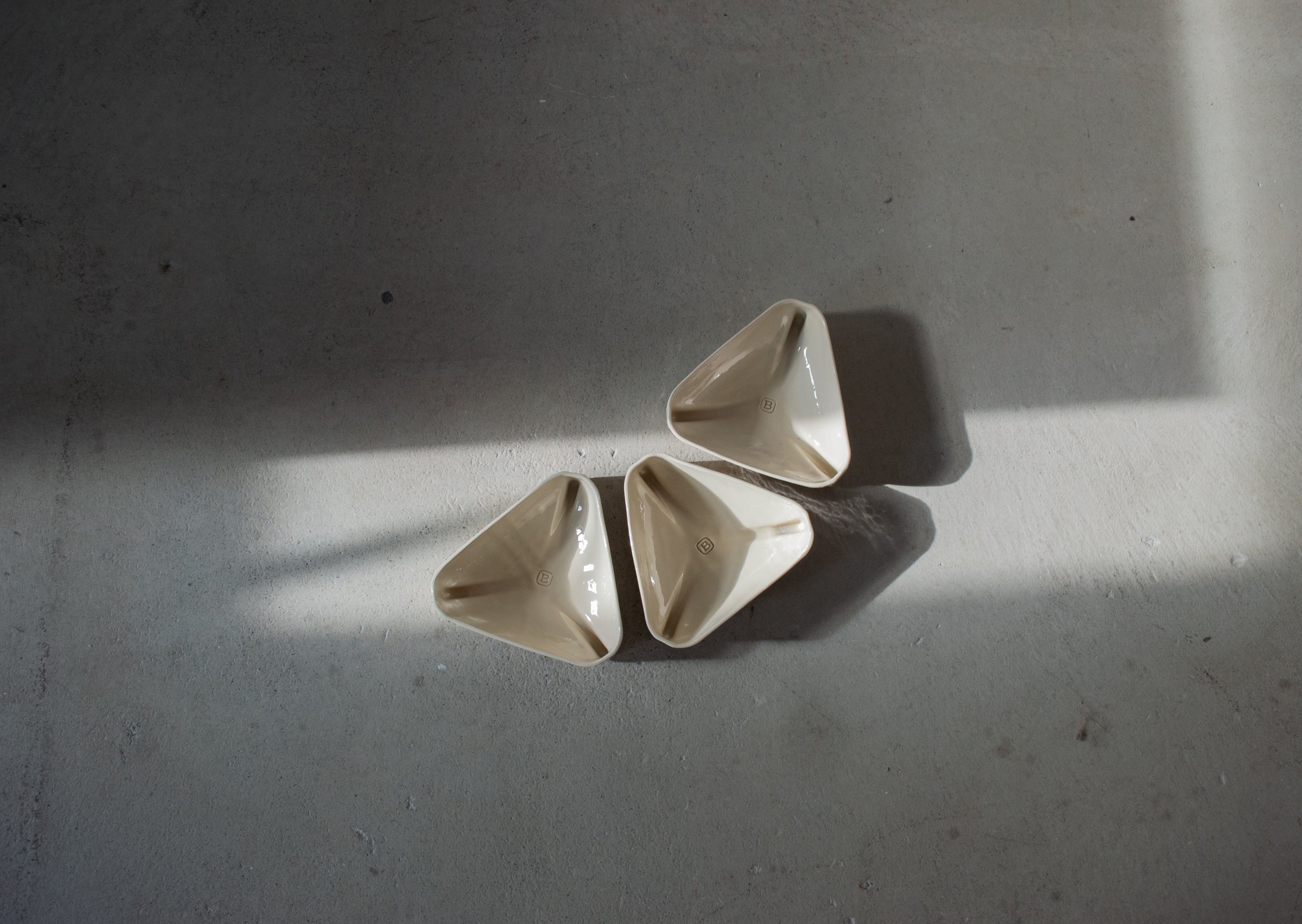 Top view of three triangular ceramic bowls with glossy cream glaze on concrete floor