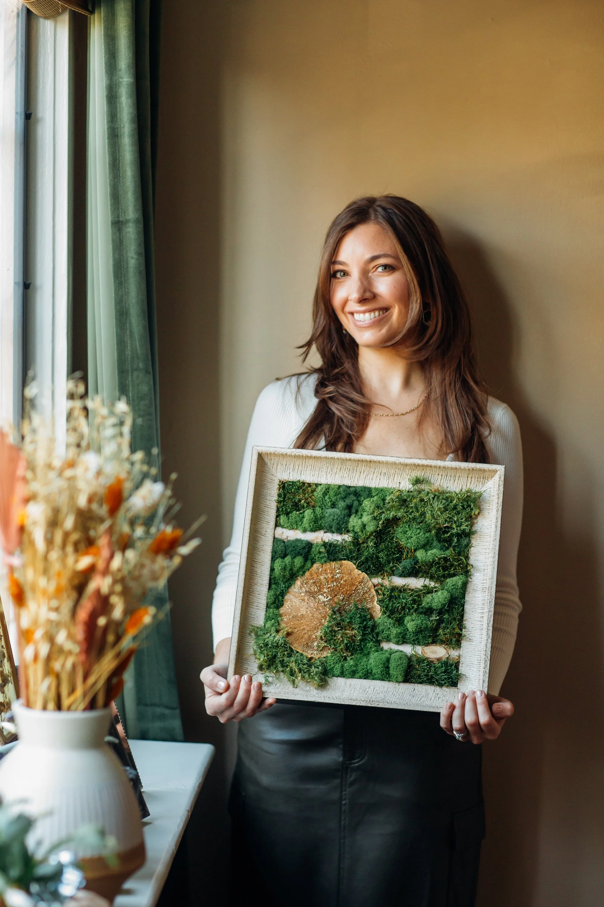 Ally Amenta artist holding botanical art with greenery mushrooms looking at the camera