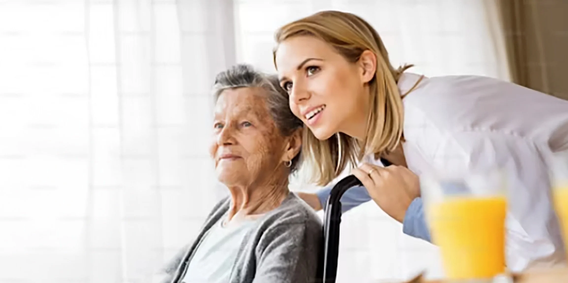 A caregiver smiling next to an elderly woman in a cozy setting.