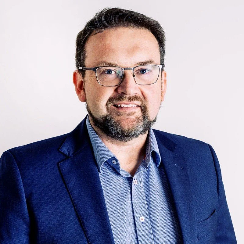 Smiling person with short hair wearing a checkered shirt against a white background.