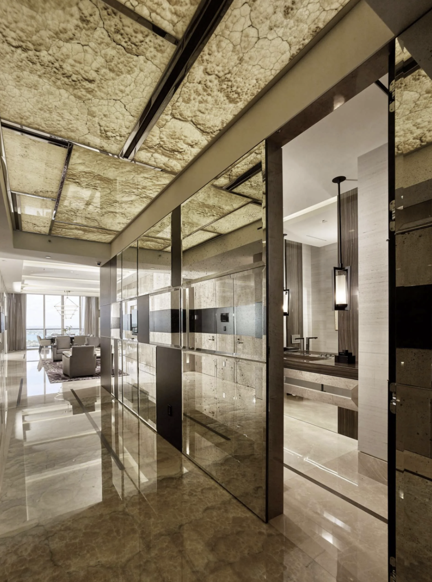 Elegant modern hotel interior with marble flooring, glass partitions, and a view of a living area with large windows overlooking the ocean.