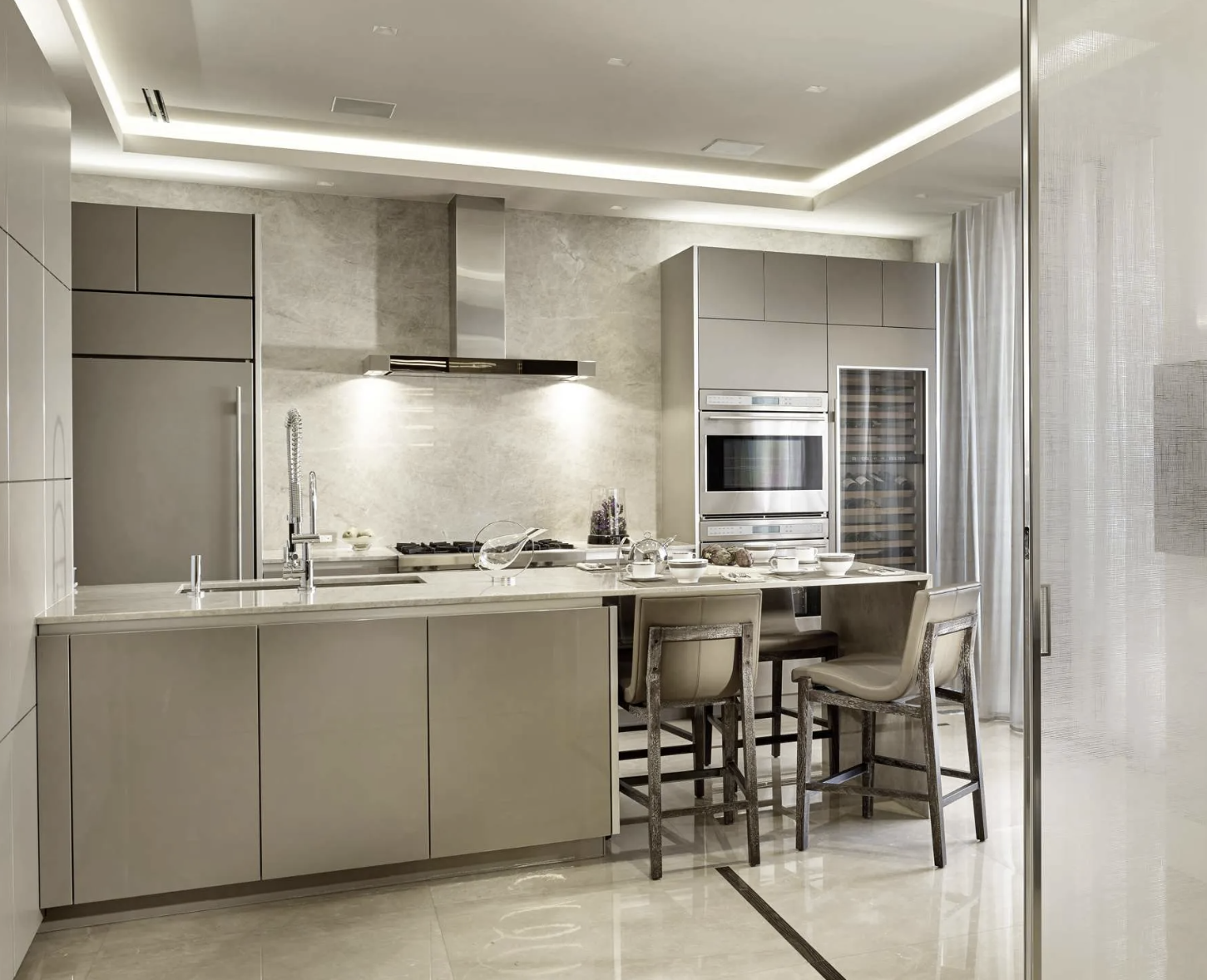 Modern kitchen with beige cabinets, a marble island, stainless steel appliances, and a dining area with four chairs and a table set for a meal.