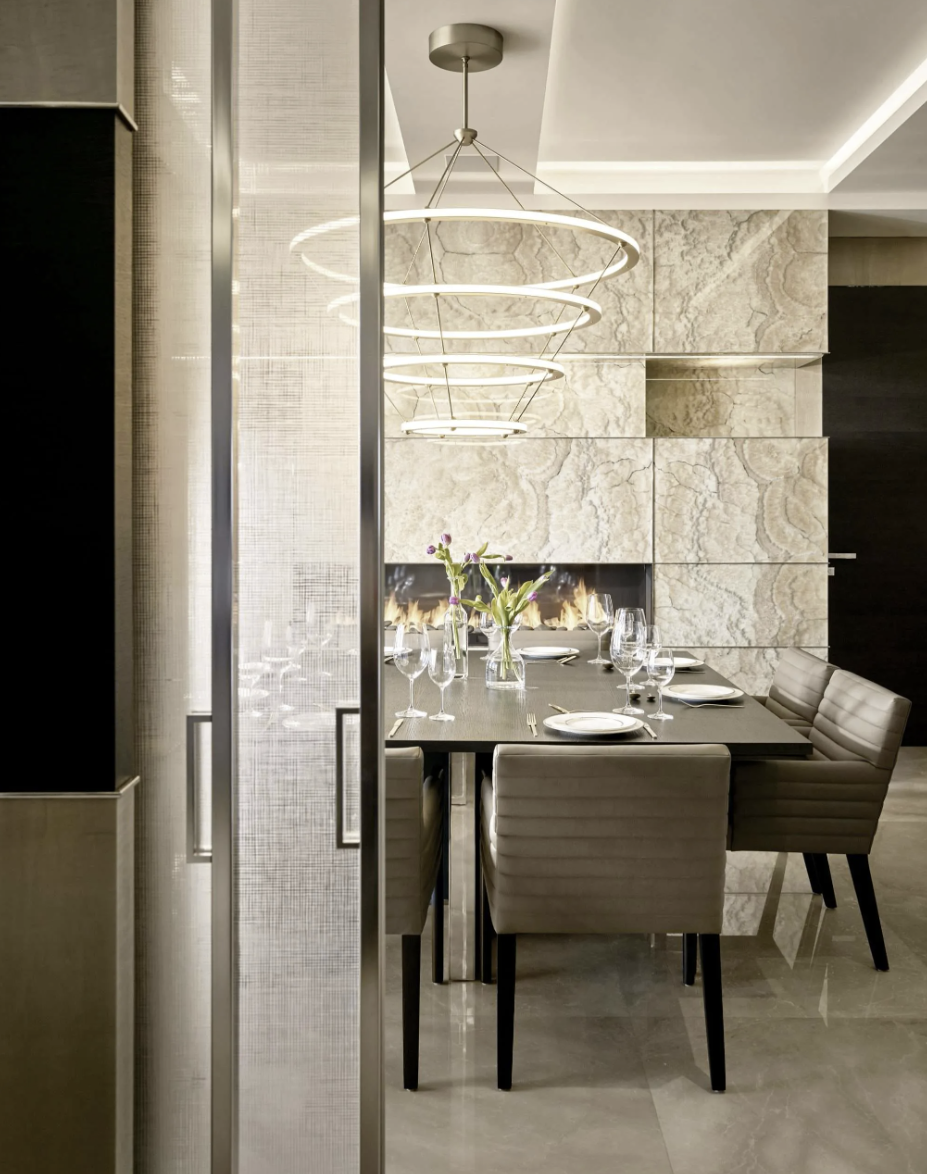 A modern dining room with a dark wood table set with plates, glasses, and a vase of flowers, surrounded by beige upholstered chairs, and illuminated by a contemporary circular pendant light fixture.