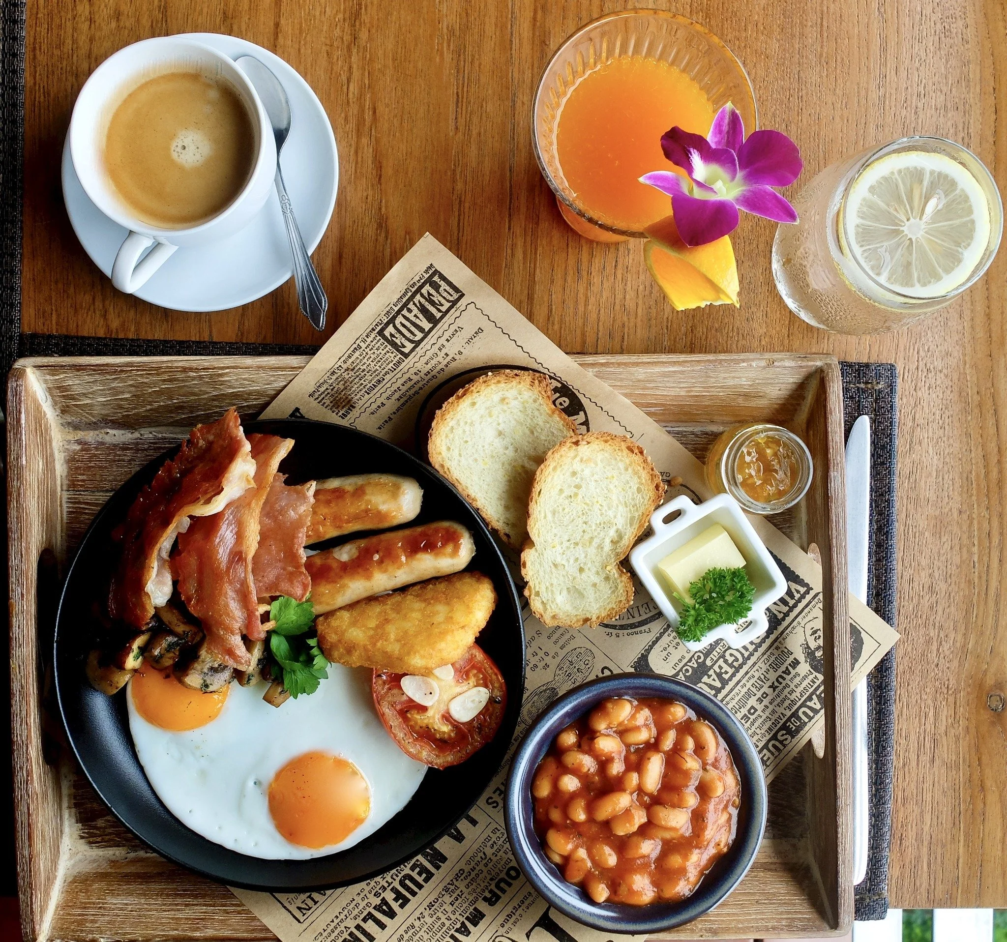 Breakfast with fried eggs, bacon, toast, baked beans, and coffee. Refreshing orange juice and lemon water on a wooden table.
