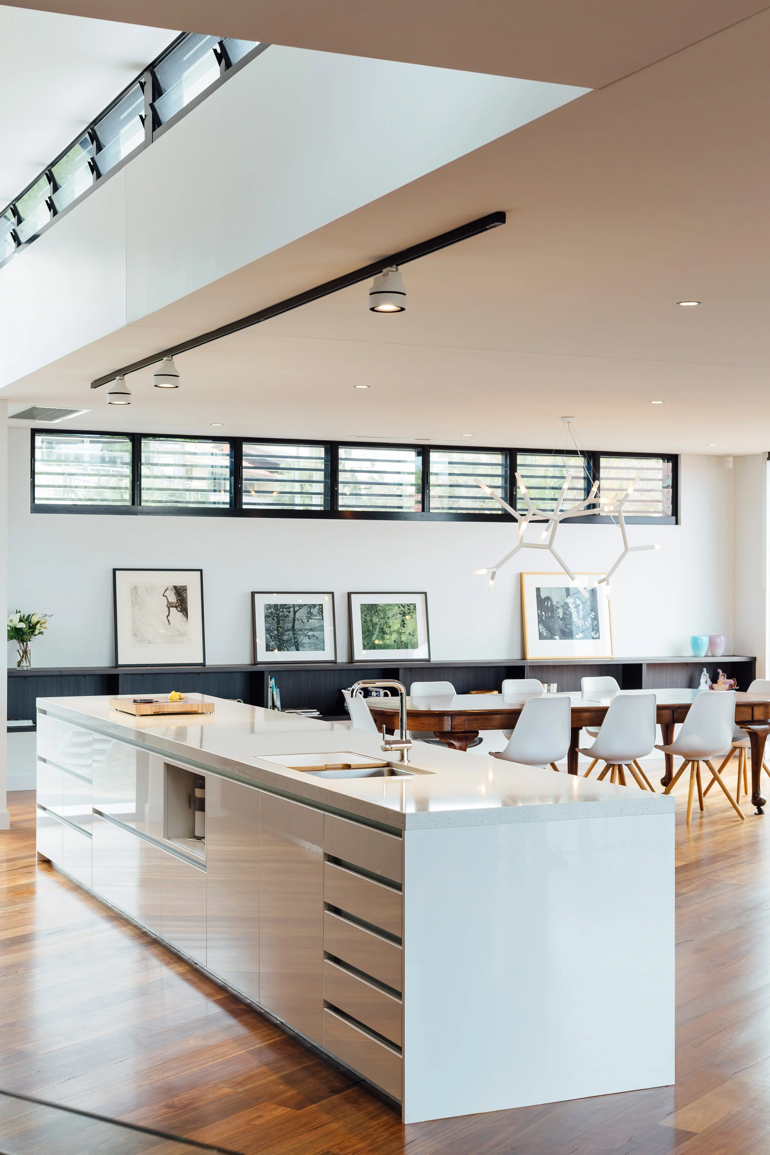 Modern kitchen with a white island, wooden flooring, a black backsplash, and framed artwork on the wall. Large windows provide natural light.