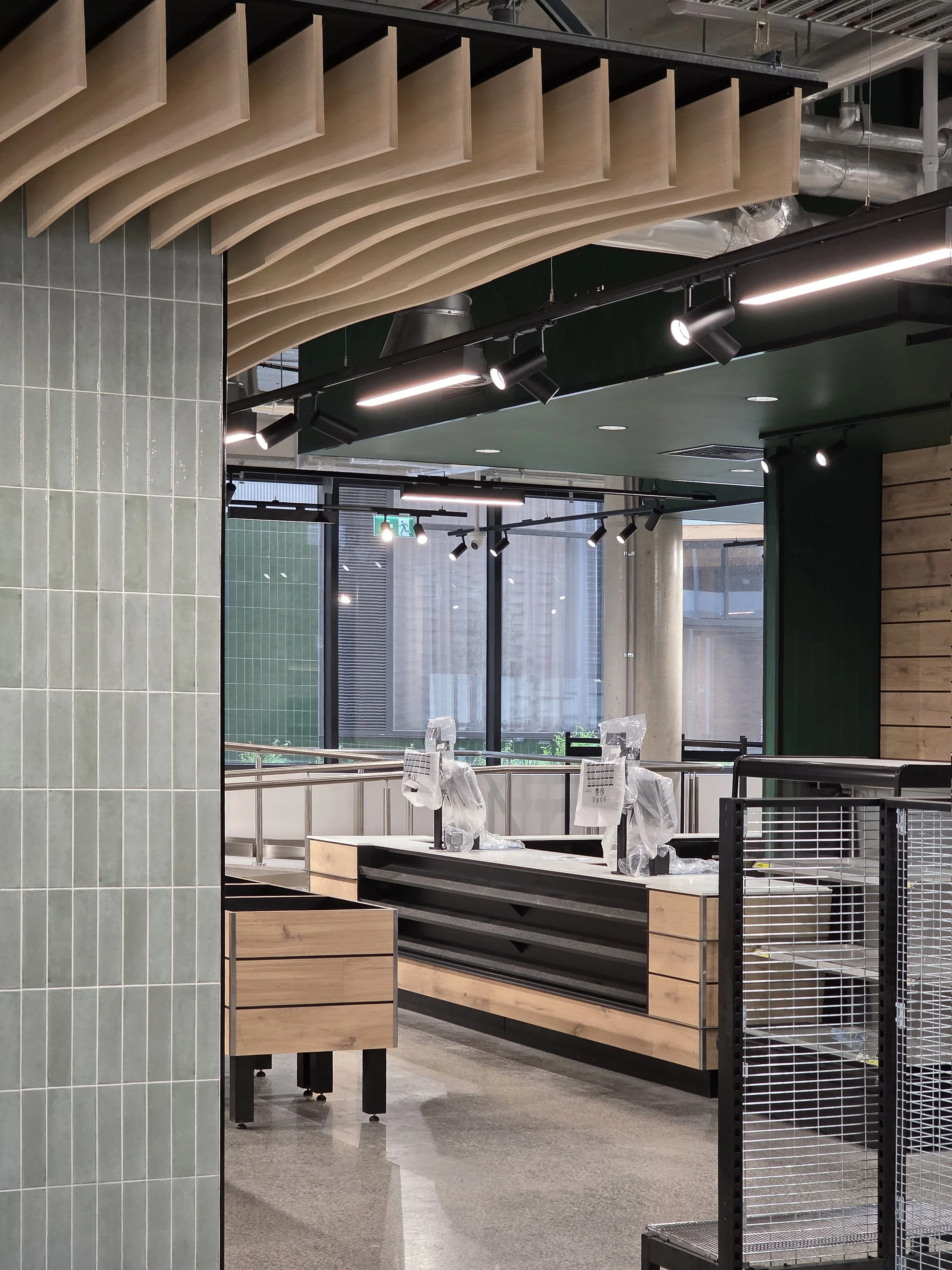 Empty retail store under construction with wooden display tables, metal shelves, a tiled wall, and overhead lighting.