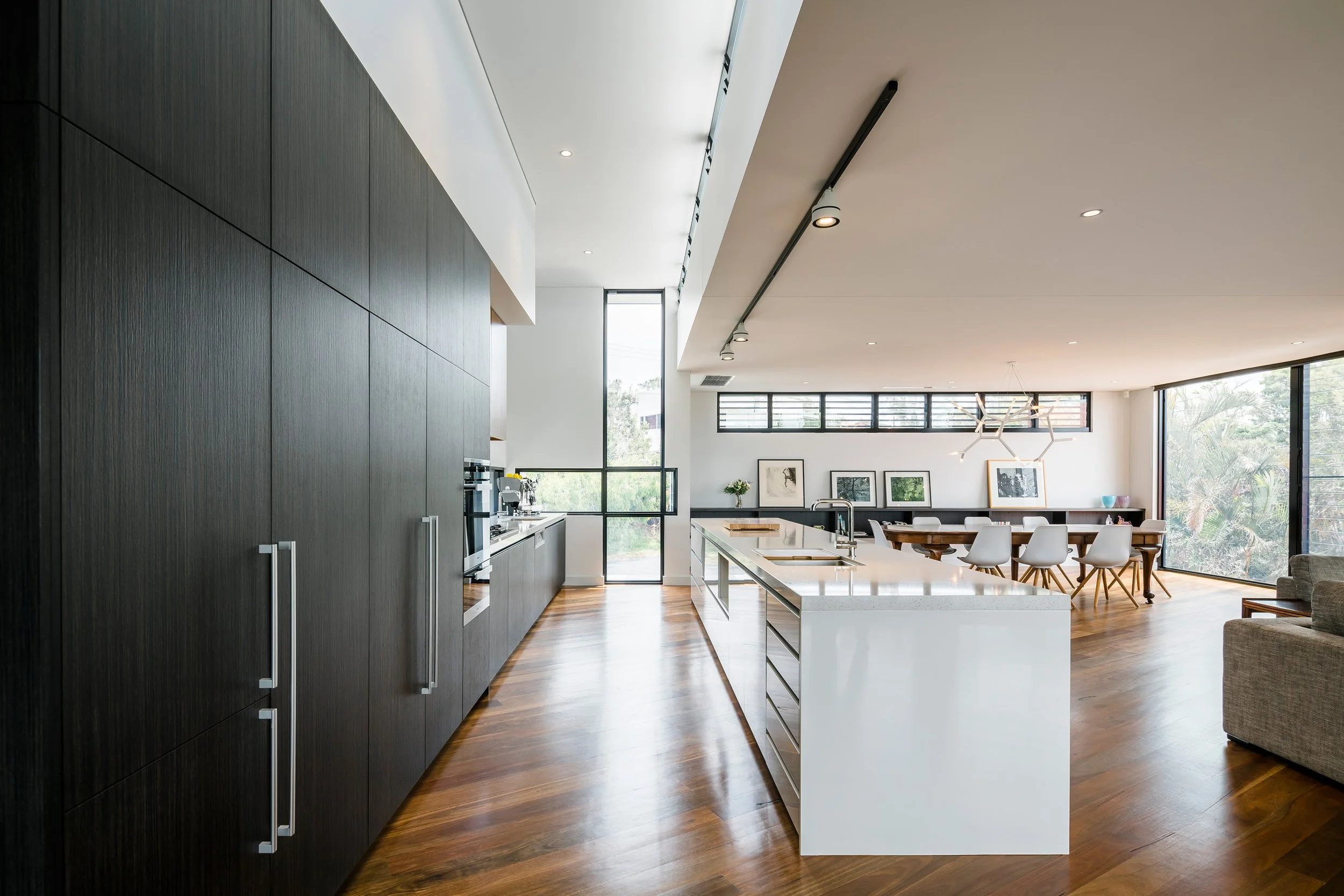 Modern open-concept kitchen and dining area with large windows, white island, black cabinetry, and minimalist decor.