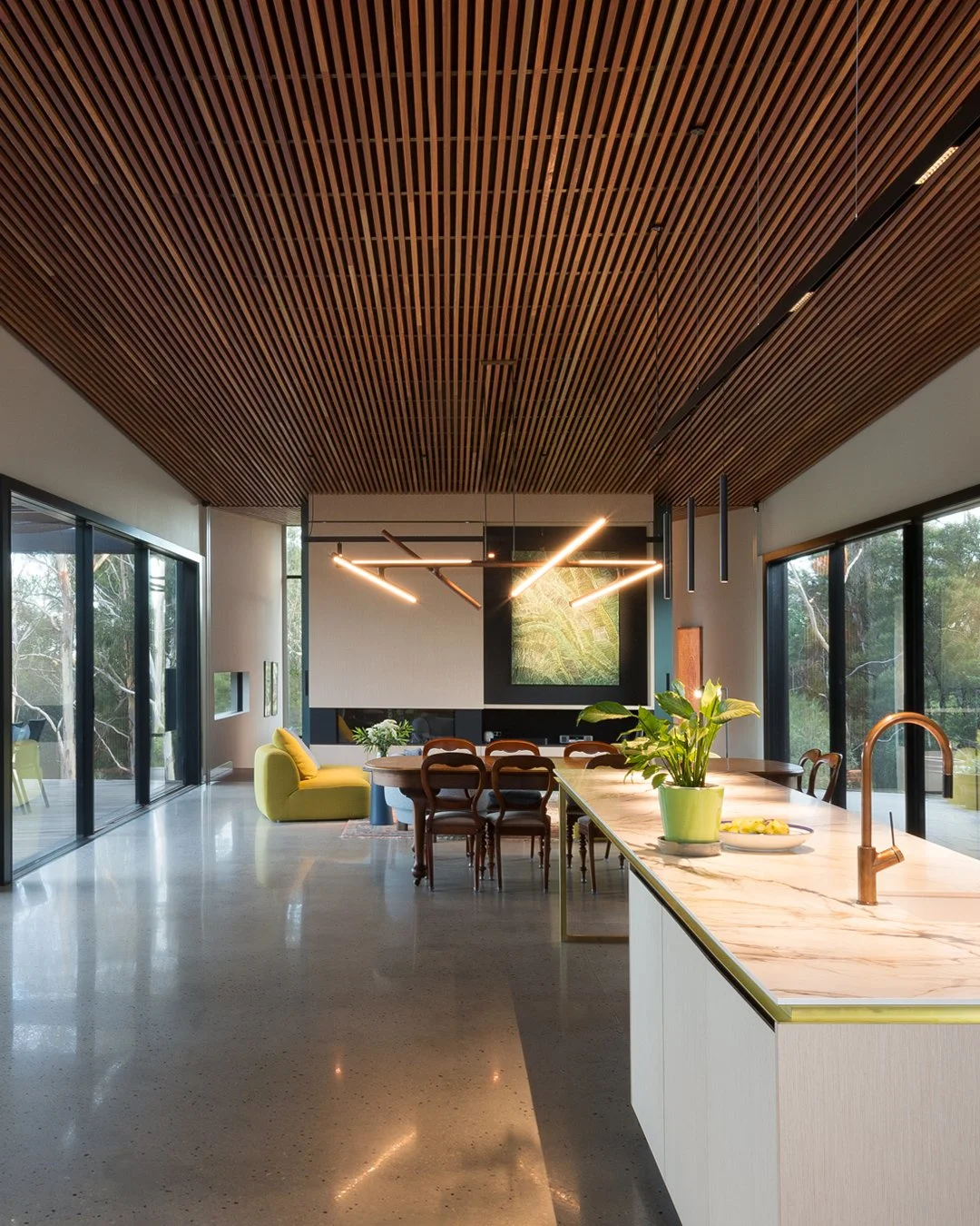 Modern open-concept kitchen and dining area with wooden ceiling, marble countertop, large windows, and minimalist decor.