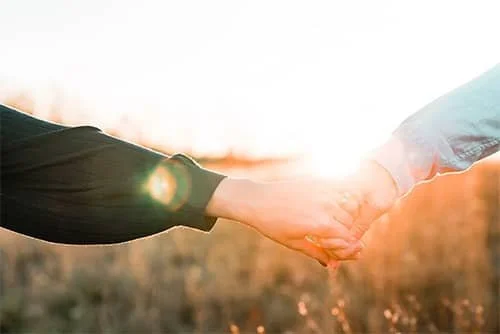 Two people holding hands in warm sunlight.