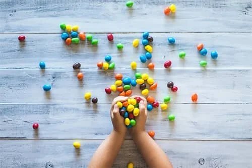 Child reaching toward colorful beads on a wooden floor.