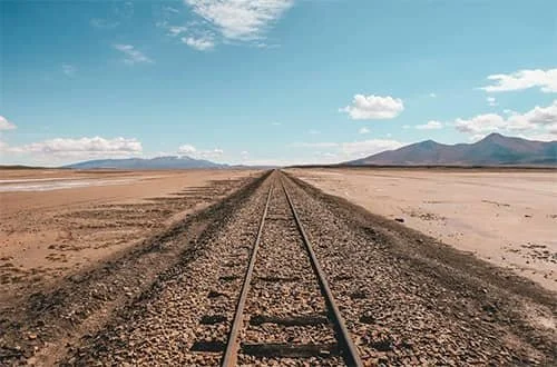 Empty railroad tracks stretching across a desert landscape.
