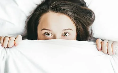 Person lying in bed with eyes open above the blanket.
