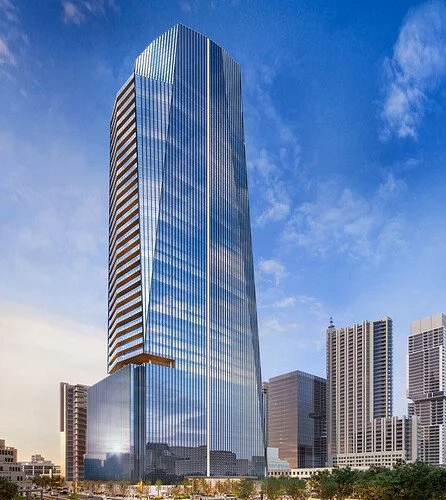 Tall glass skyscraper with vertical design, surrounded by other buildings, under blue sky.