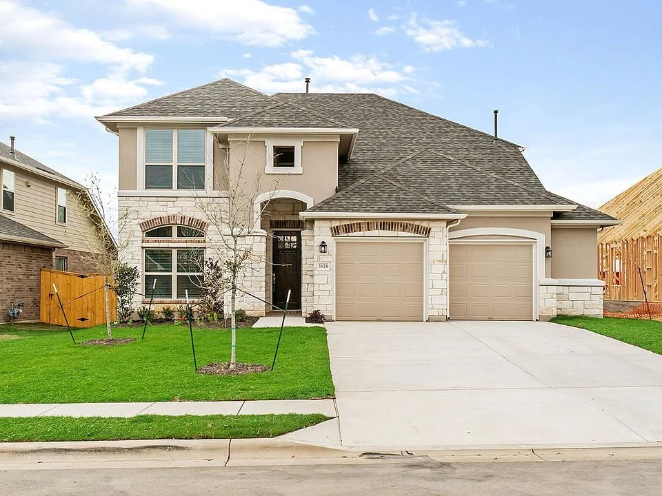 Two-story suburban house with double garage, brick and stone facade, manicured lawn, and a driveway.