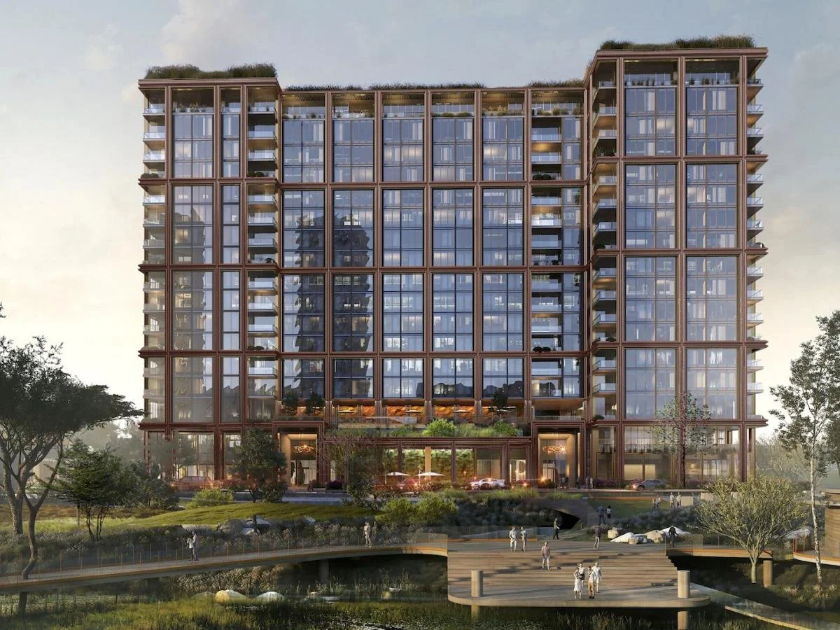 A modern multi-story glass building with outdoor greenery and trees in the foreground.