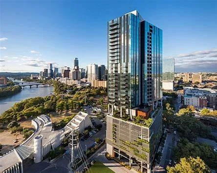 Skyline view of a tall modern building in a city with a river and other high-rise buildings in the background.