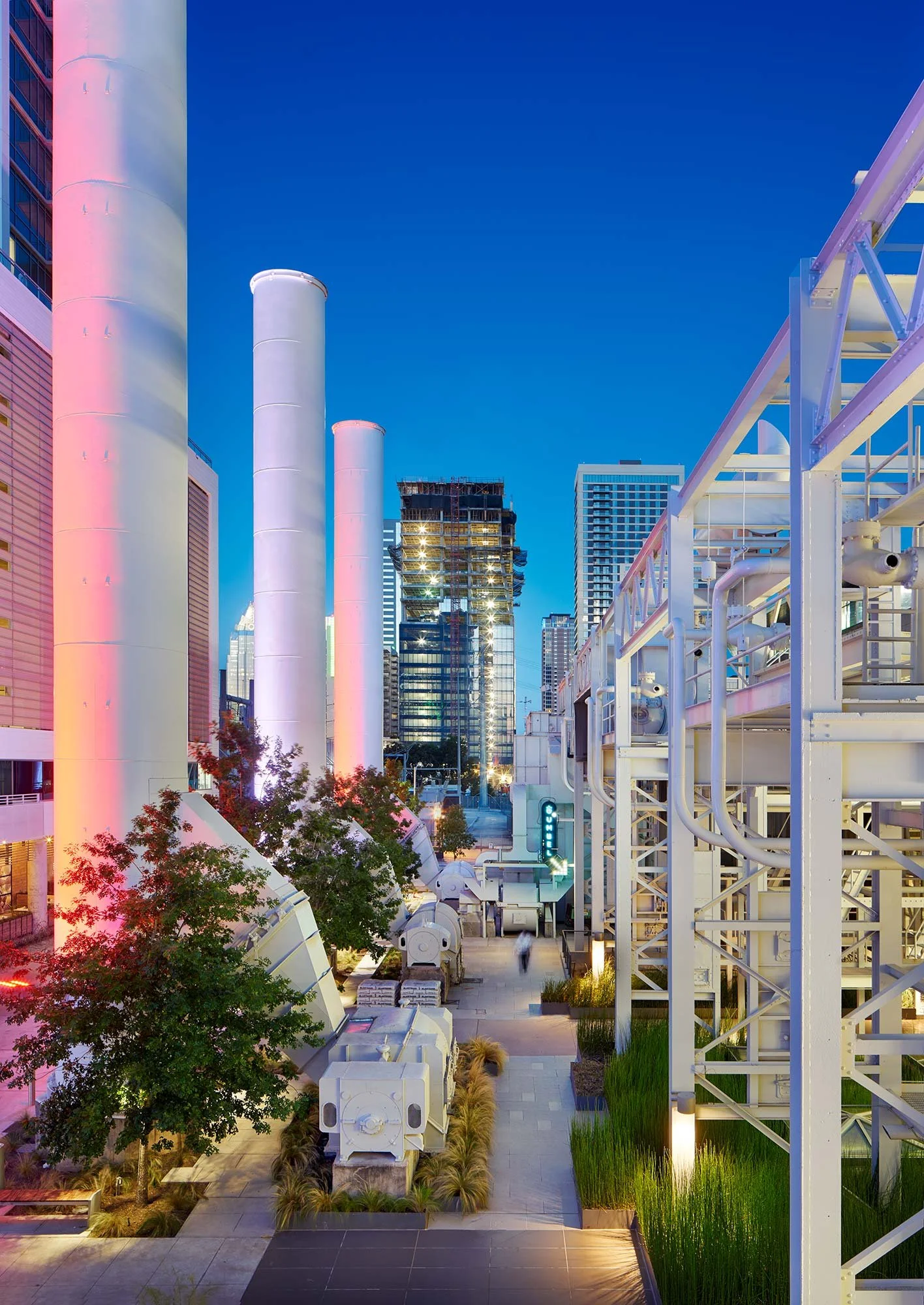 Night view of an urban area with industrial equipment, pipes, and tall buildings illuminated in the cityscape.