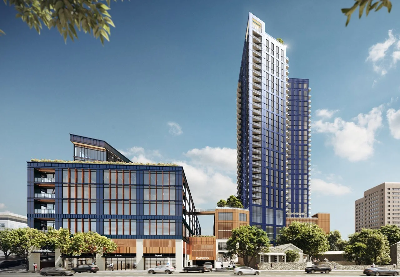 A modern cityscape featuring a tall, glass skyscraper with a blue tint and other mid-rise buildings with commercial spaces on the ground floor, trees lining the street, and cars driving by under a clear sky.