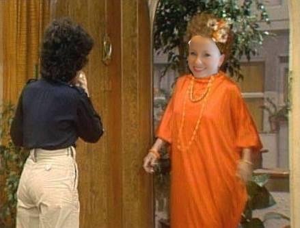 Person in an orange costume entering a room, greeted by another person.