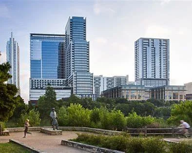 City skyline with modern high-rise buildings and a park in the foreground with people walking and sitting.