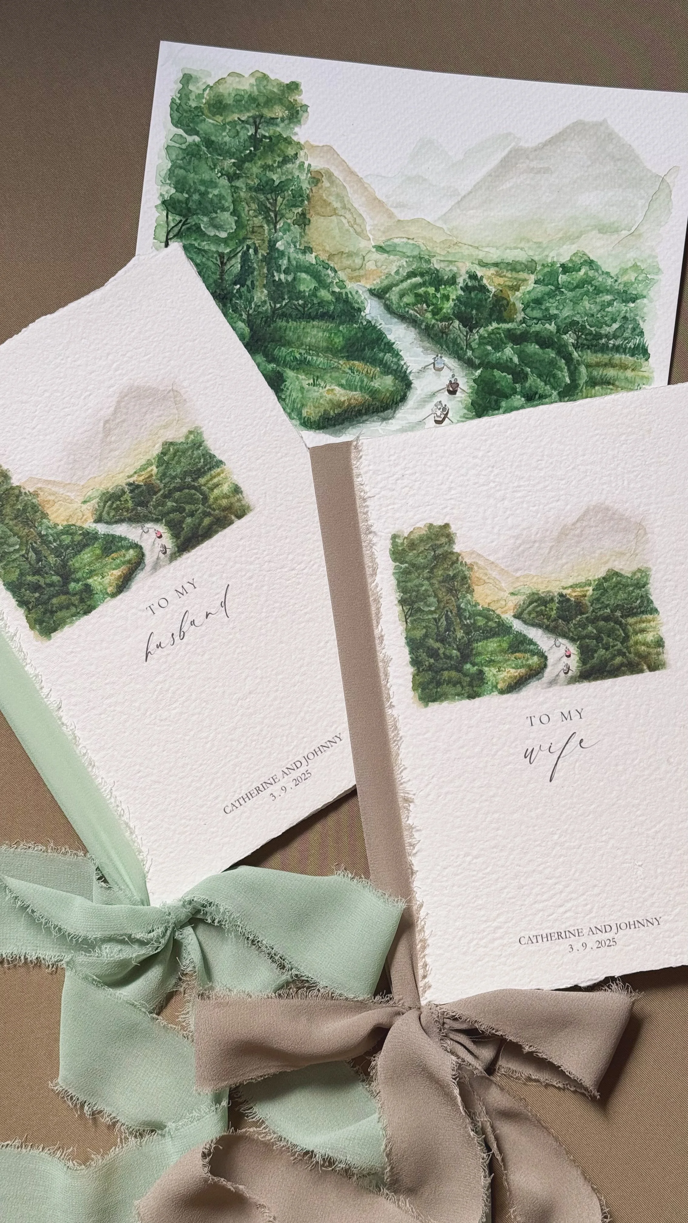 Watercolor paintings of a lush green river landscape with mountains in the background, on textured paper. Two of the paintings are on greeting cards, one for a husband and one for a wife, both dated March 9, 2025, signed by Catherine and Johnny, with pastel-colored ribbons.