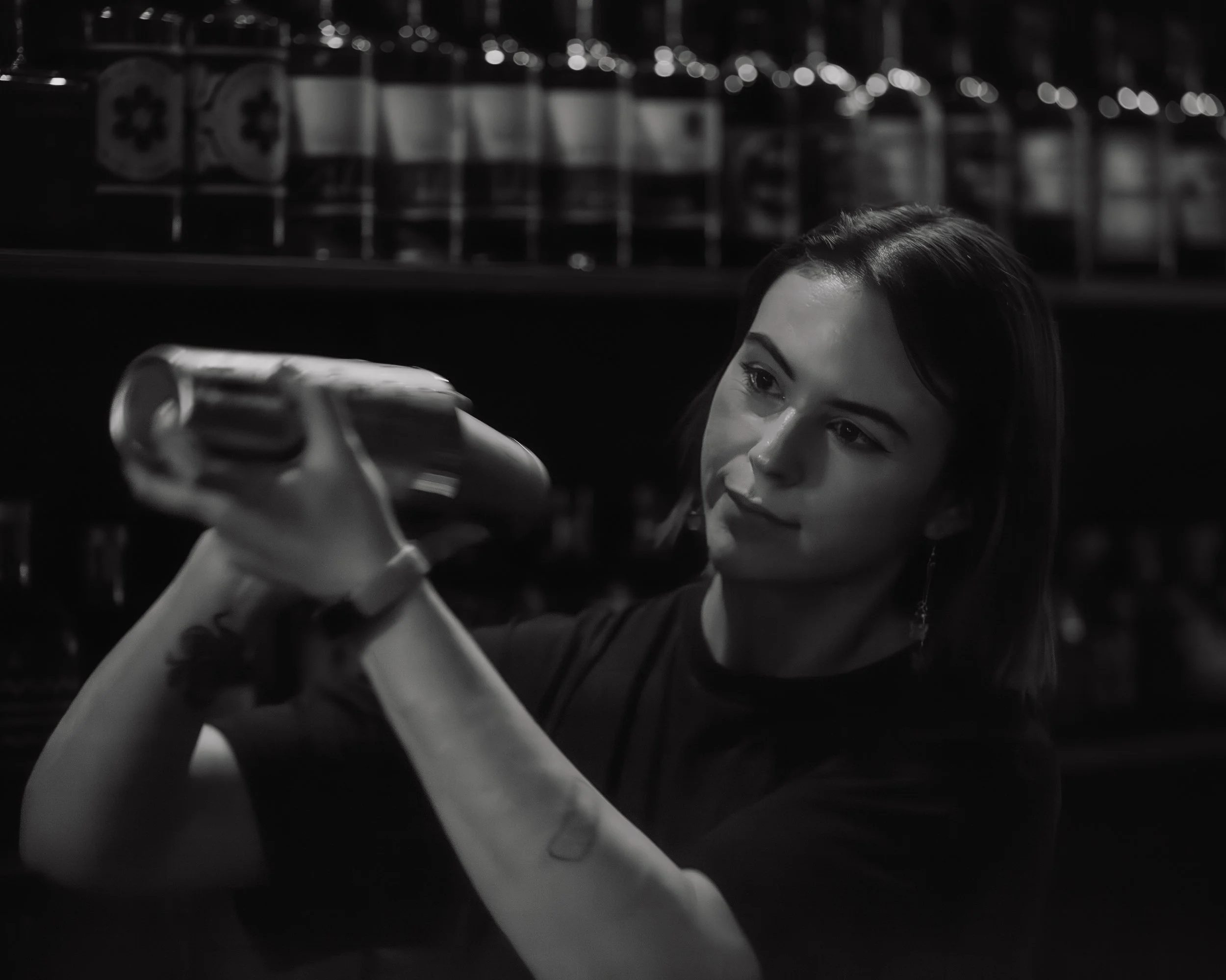 A woman with dark hair and earrings looking at her phone in a dimly lit environment, possibly a bar or a nightclub, in black and white.