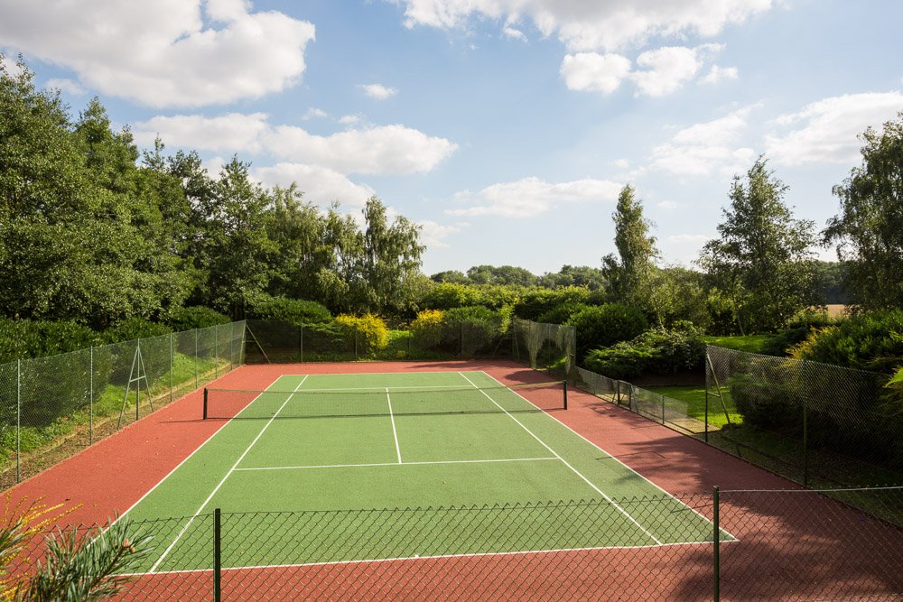 high fenced tennis court surrounded by tall trees and hedges  